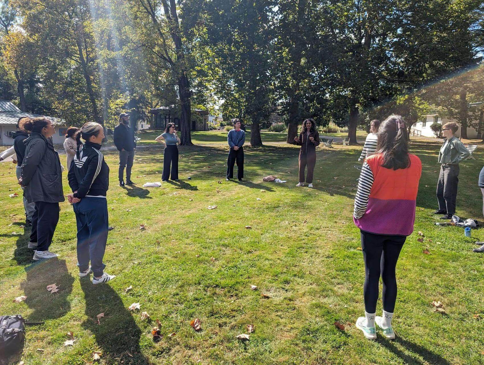 Three people seated on lawn chairs in a grassy area, surrounded by trees and a building.