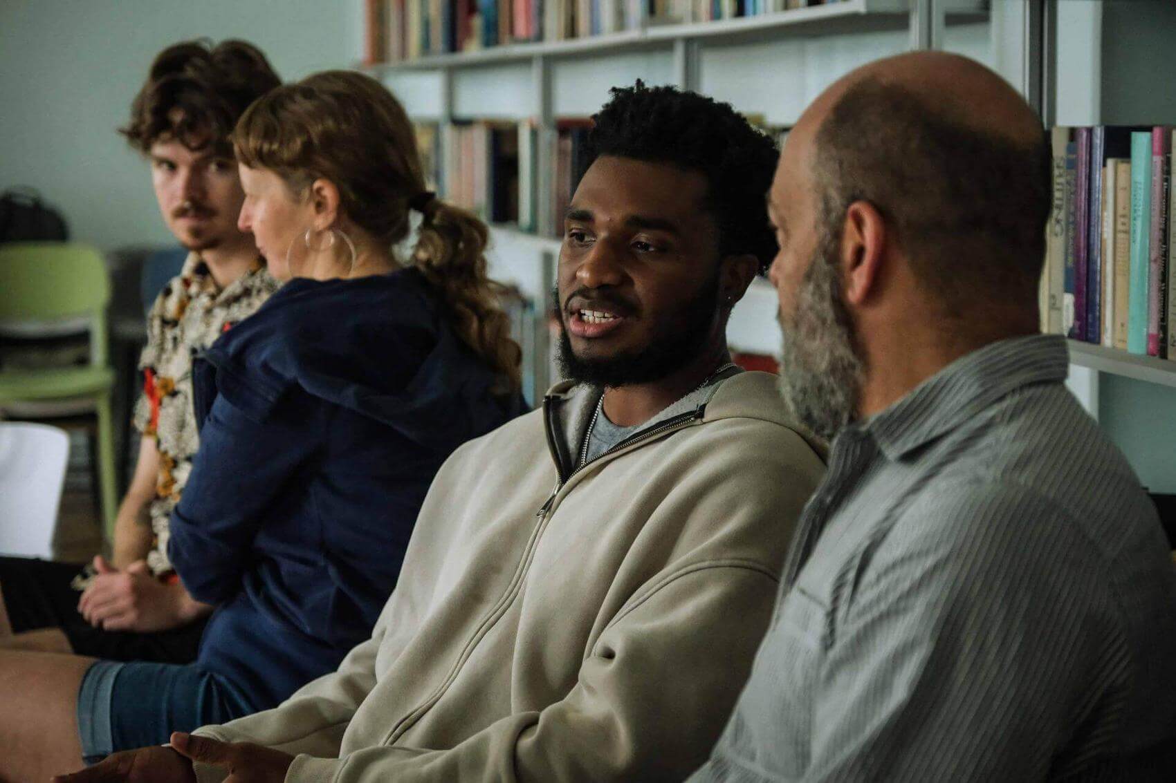 A man and a woman are engaged in conversation, with shelves of books in the background.