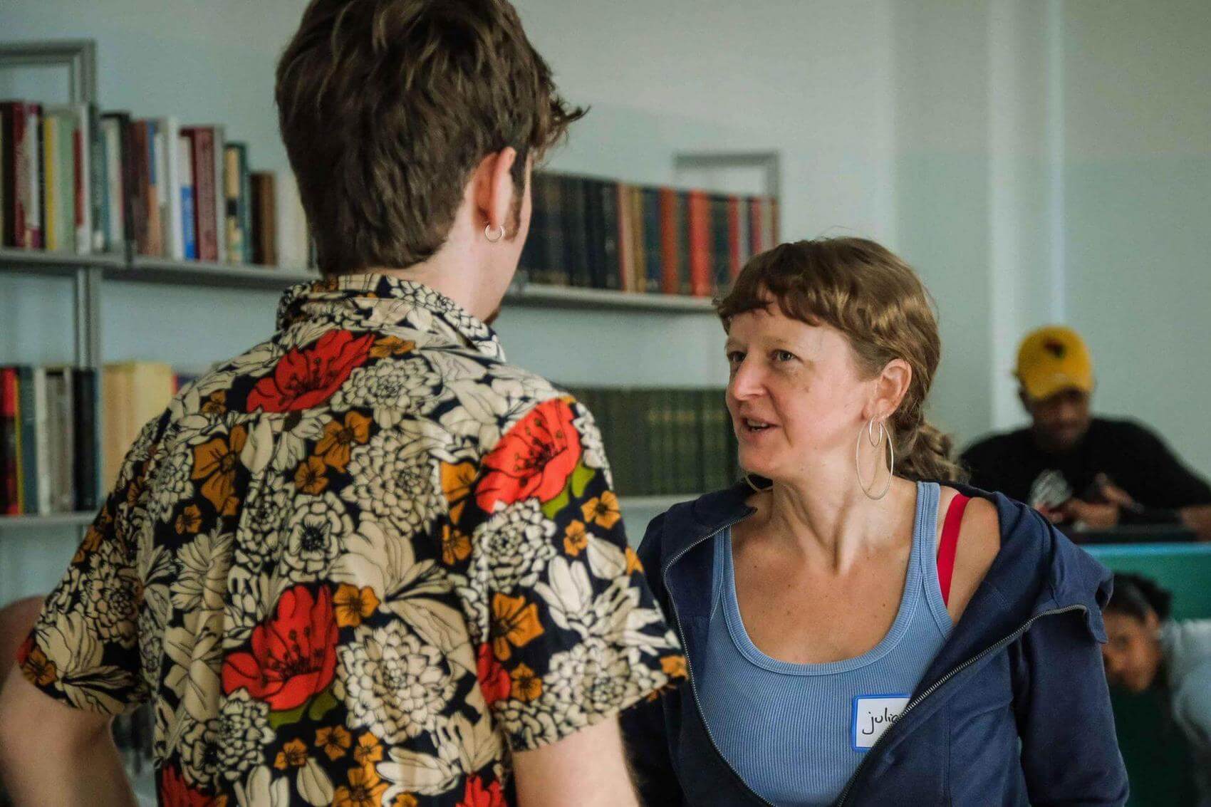 A young woman smiling in a conversation, in a room with many other young people talking.