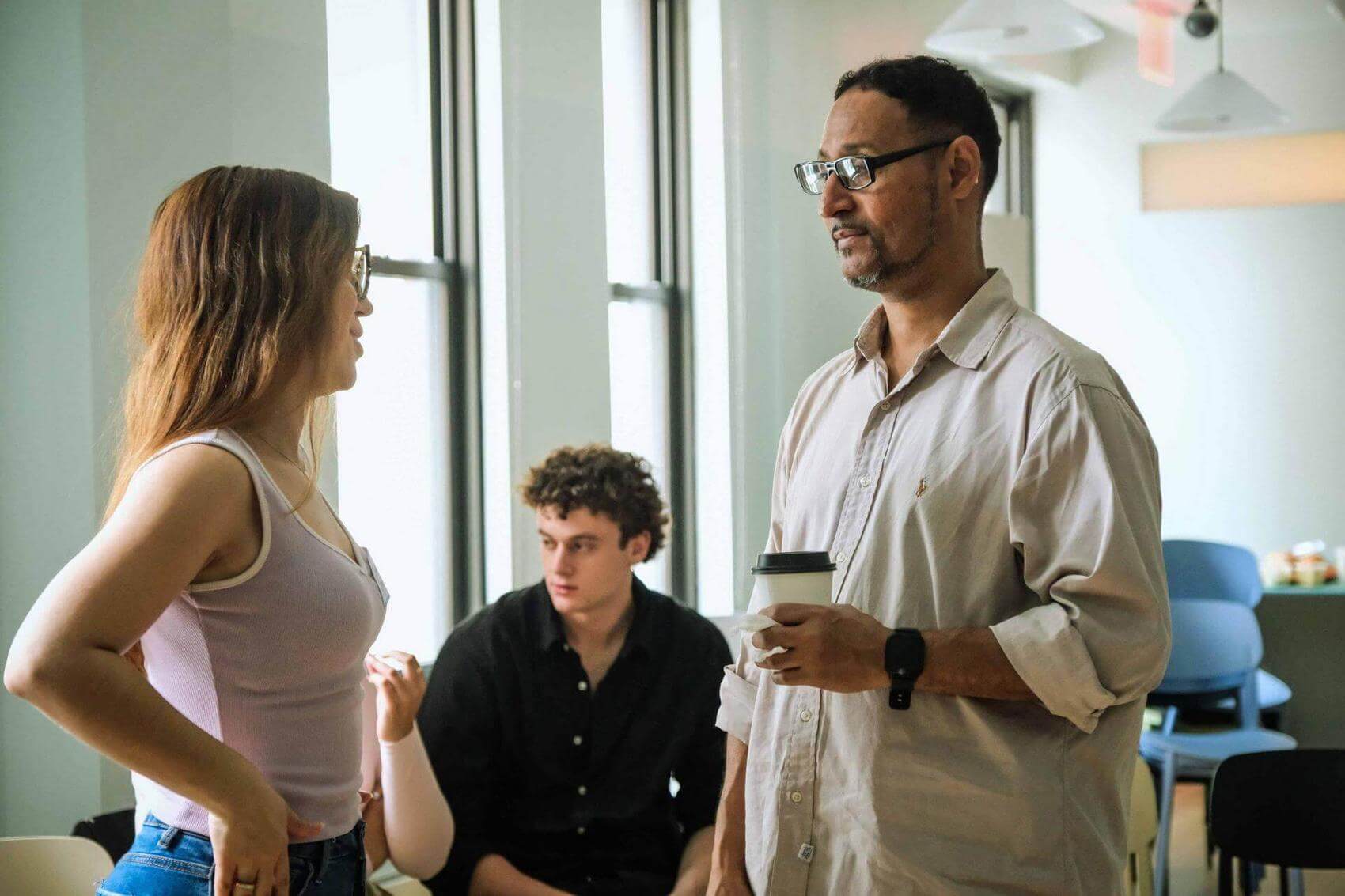 A woman talks to a man while holding a coffee cup.