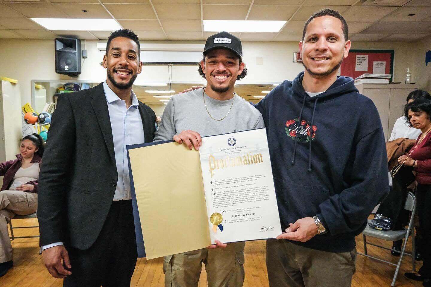 Three people seated on a stage, one speaking into a microphone while gesturing.