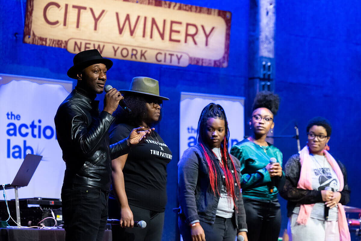 Musician on stage at City Winery with other musicians behind him, speaking to the audience