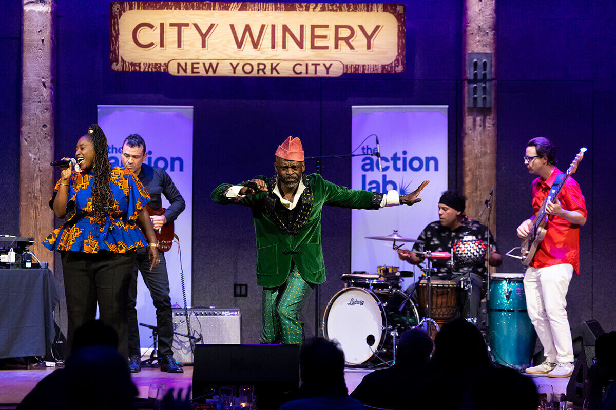 Person holding a microphone and a Wenufoye flag with blue, green, red stripes and a yellow symbol.