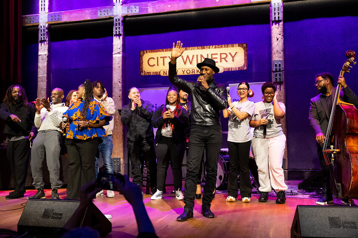 Two men fist bumping on stage, one holding a microphone and the other singing.