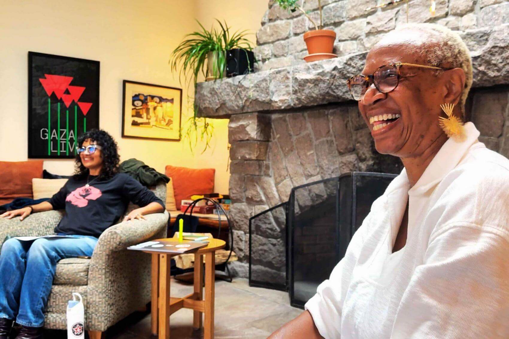 Two women sitting in a room with a stone fireplace, smiling.