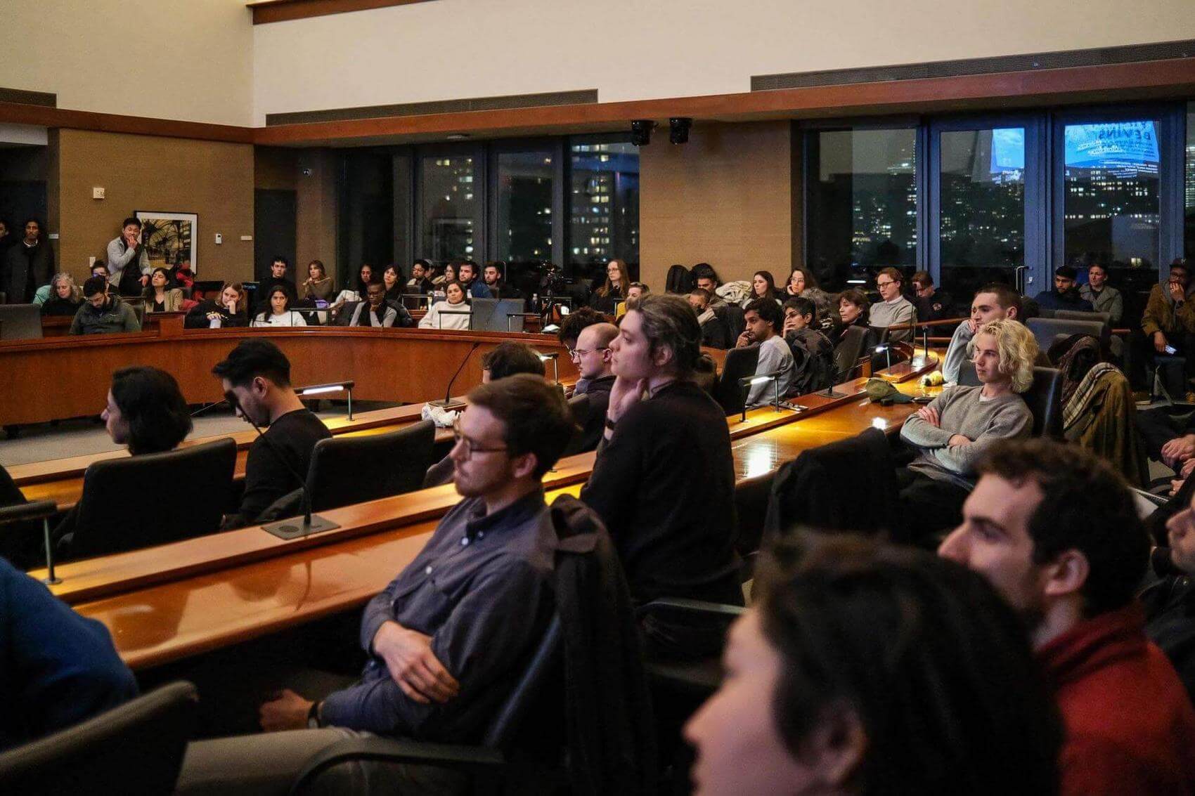 Three people seated at a table in a conference room; one gestures while speaking.