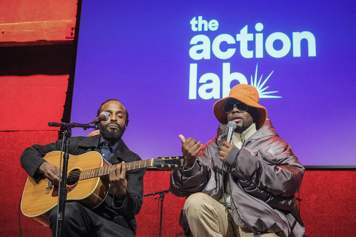 Woman singing into microphone on stage wearing patterned robe and large necklace