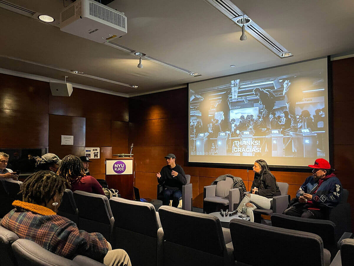 Panelists and audience members in a small conference room with a projection screen displaying "THANKS! ¡GRACIAS!" at NYU KJCC.