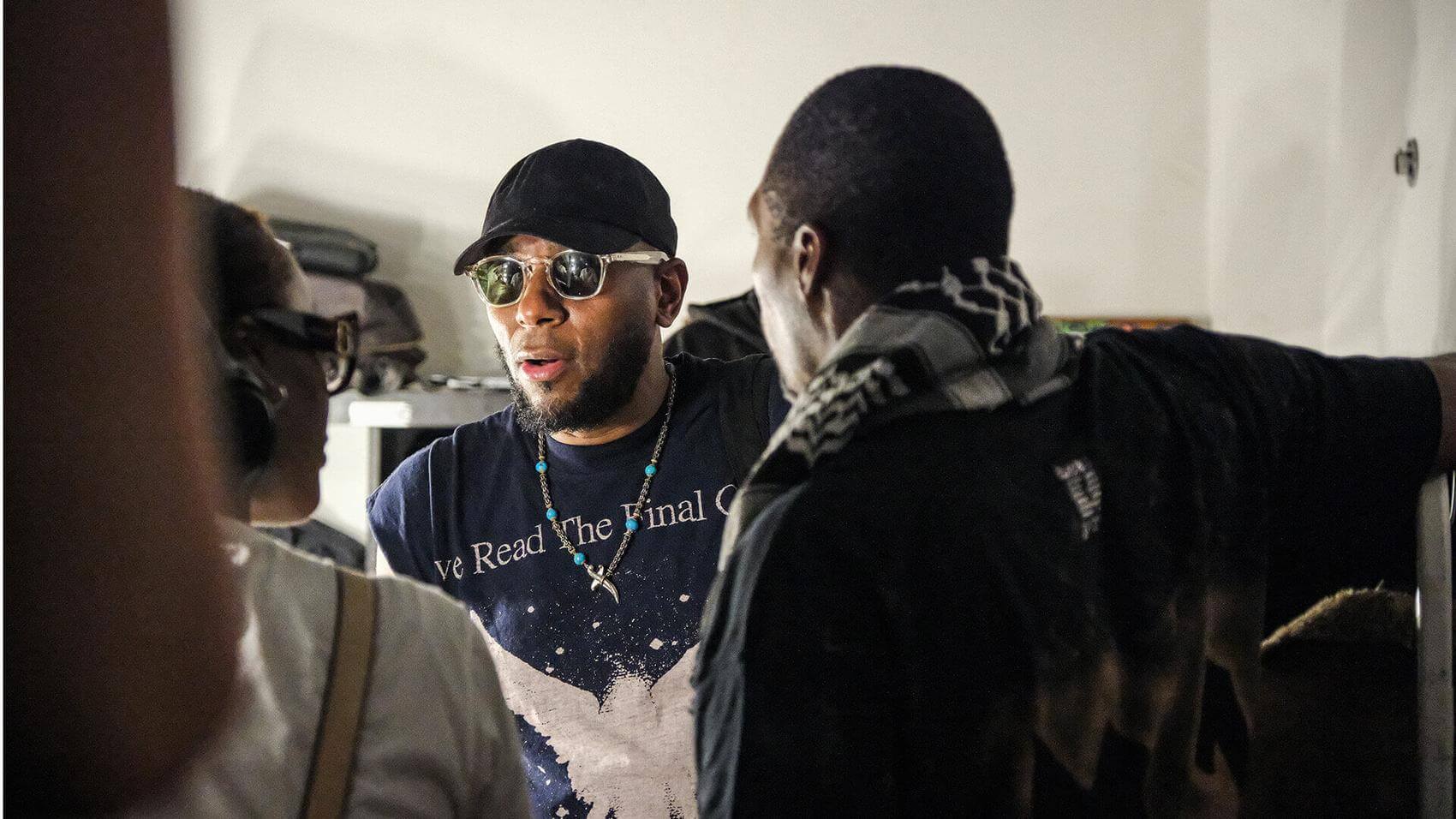 Singer holding a microphone performs on stage with colorful lighting and a backdrop.