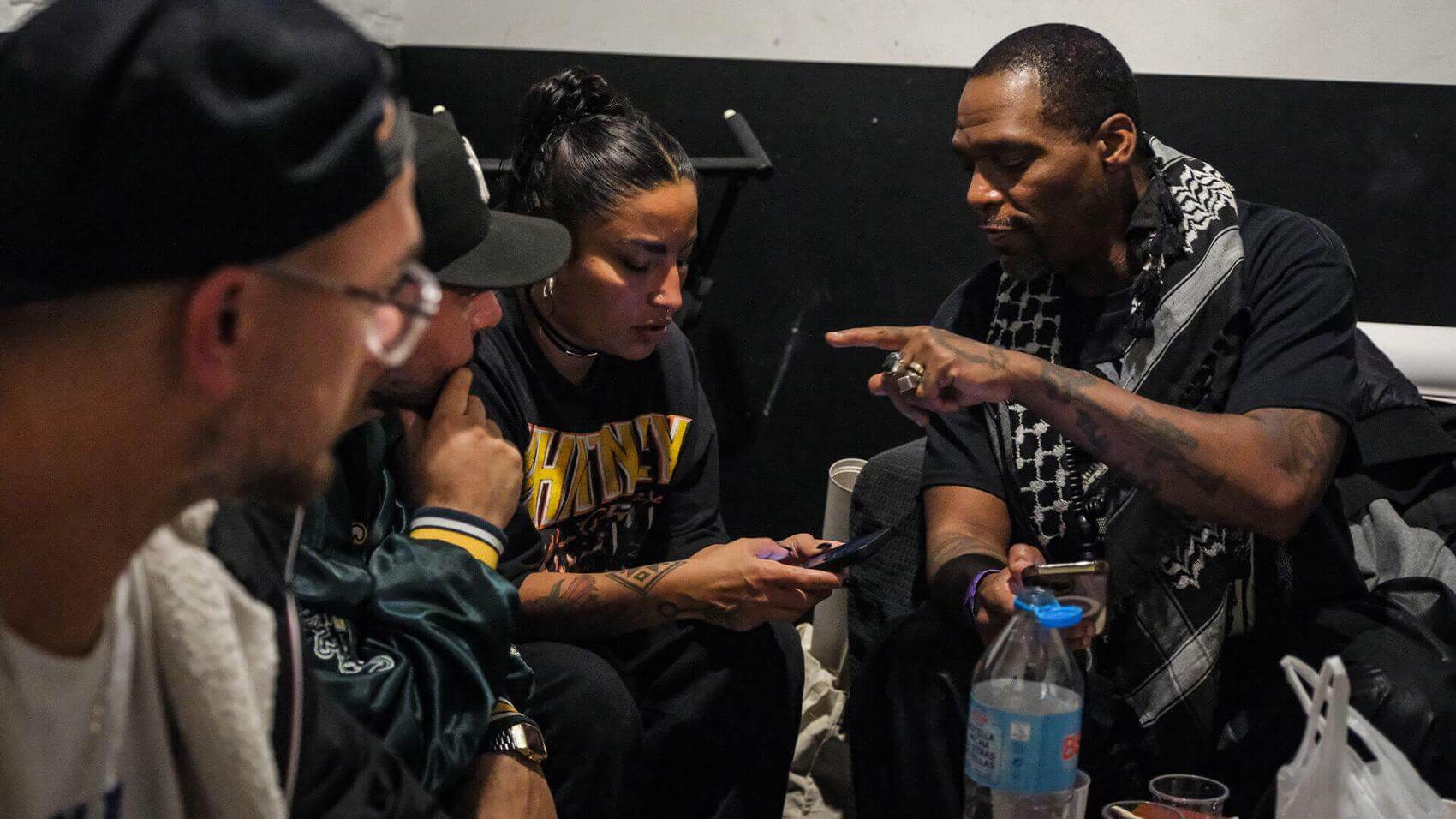 A performer on stage with an outstretched arm faces a large crowd in a dimly lit venue.