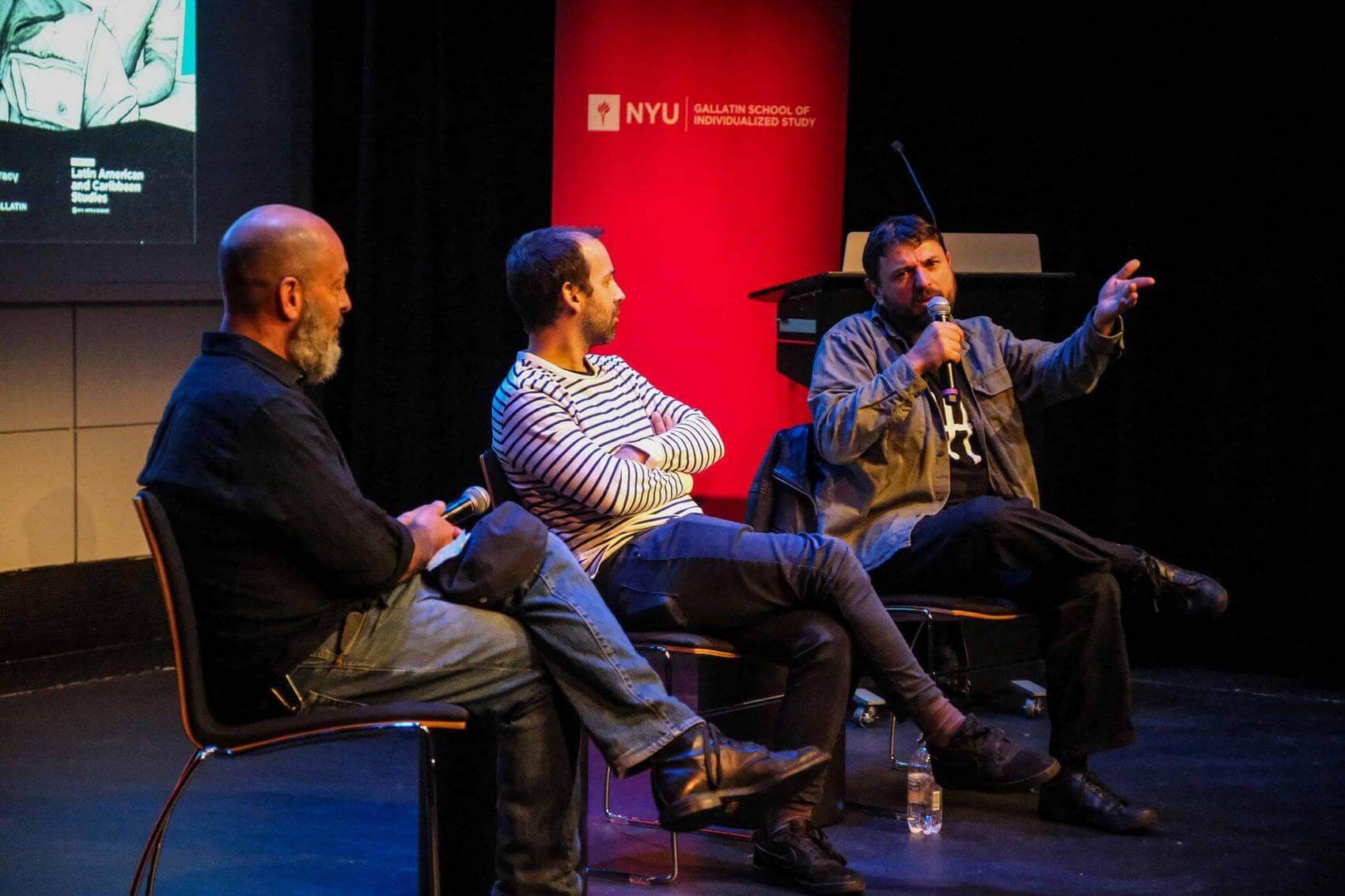 Three people seated on stage, discussing with microphones in hand. Background features a red banner with "NYU Gallatin School of Individualized Study."
