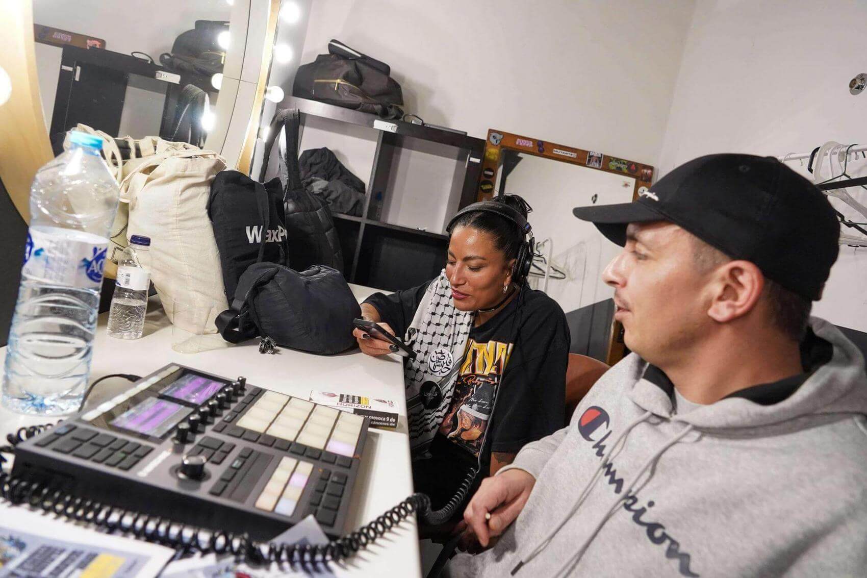 Three people engage in conversation in a dimly lit room. One person gestures while speaking.