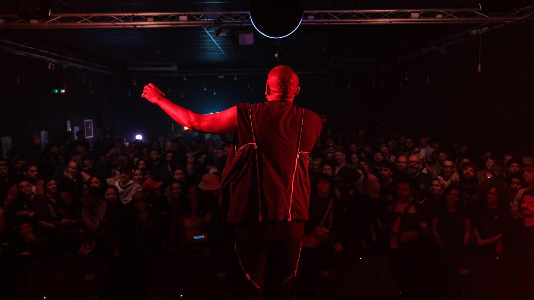 A person singing into a vintage microphone in a dimly lit space with red lighting.