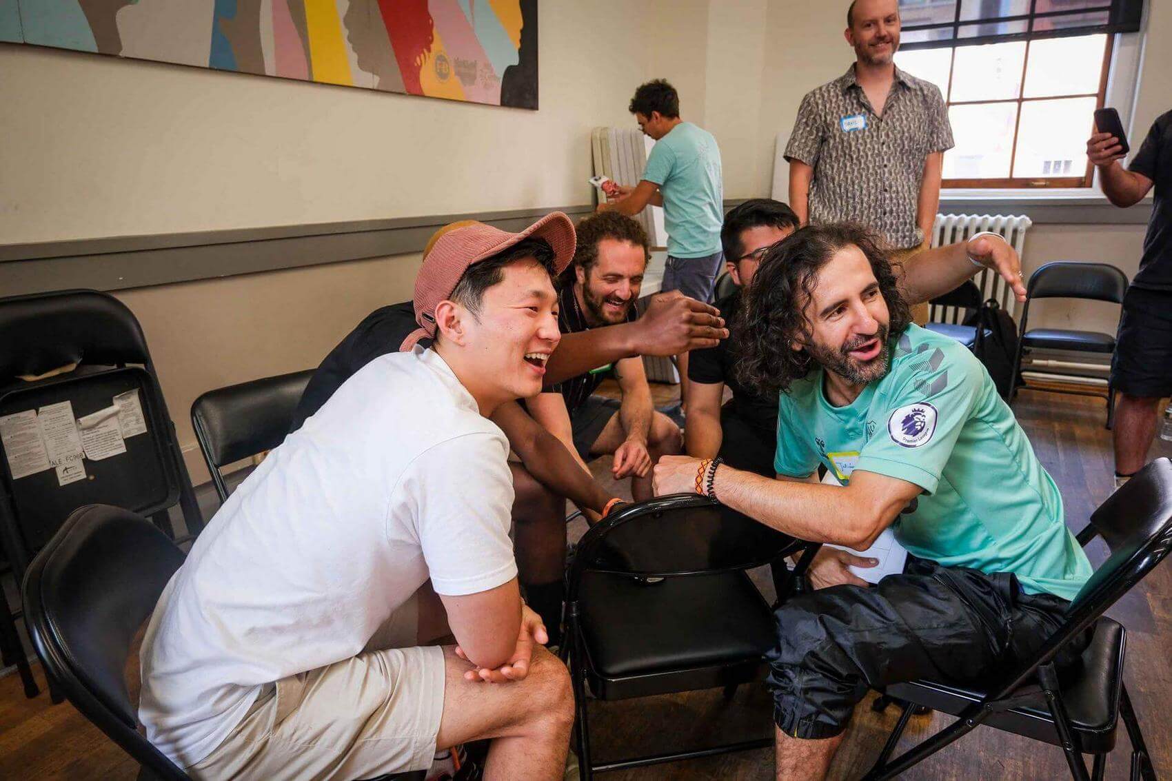 Group of men sitting and laughing around a central figure, engaged in conversation.