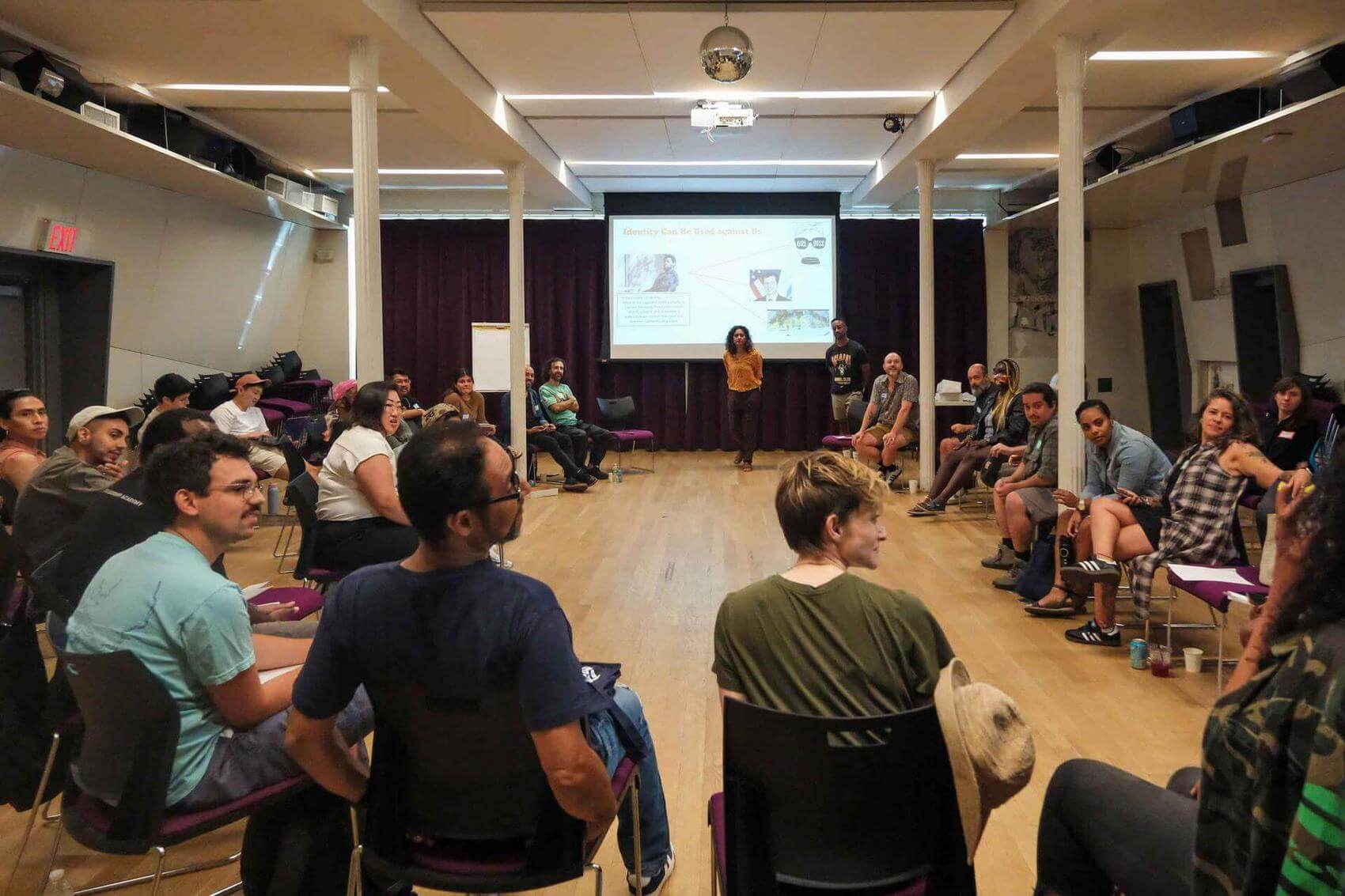 Group of people engaged in discussion in a meeting room, seated and standing in a circle.
