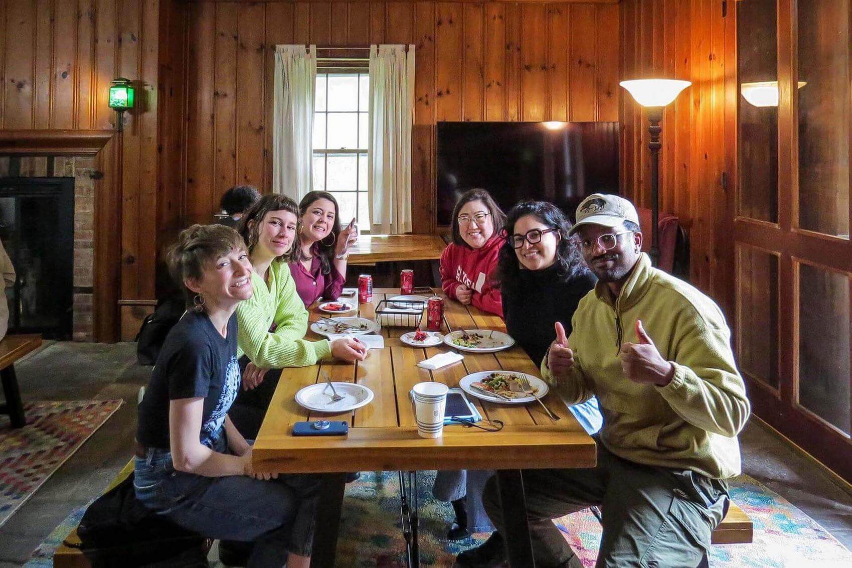 People talking and interacting in a grassy field with bare trees in the background.
