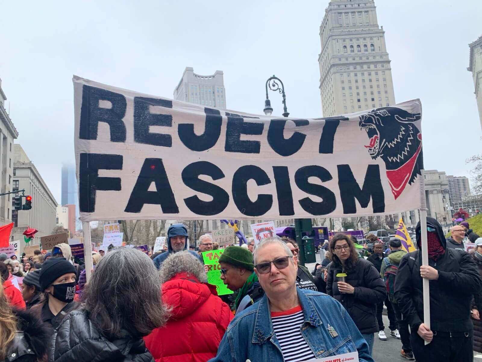 Protesters holding signs march down a city street, wearing red shirts.