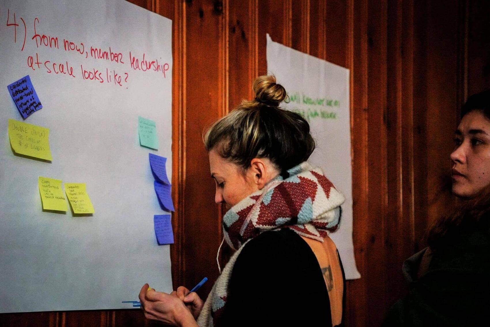 A person seated with arms raised speaks to a small group in a meeting room.