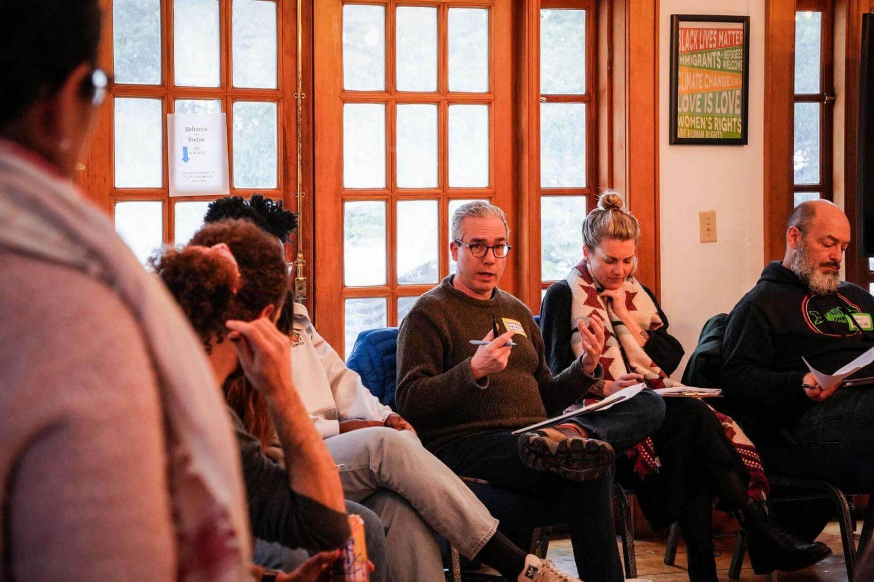 Woman writing notes in front of sticky notes on a wall, another person observing.