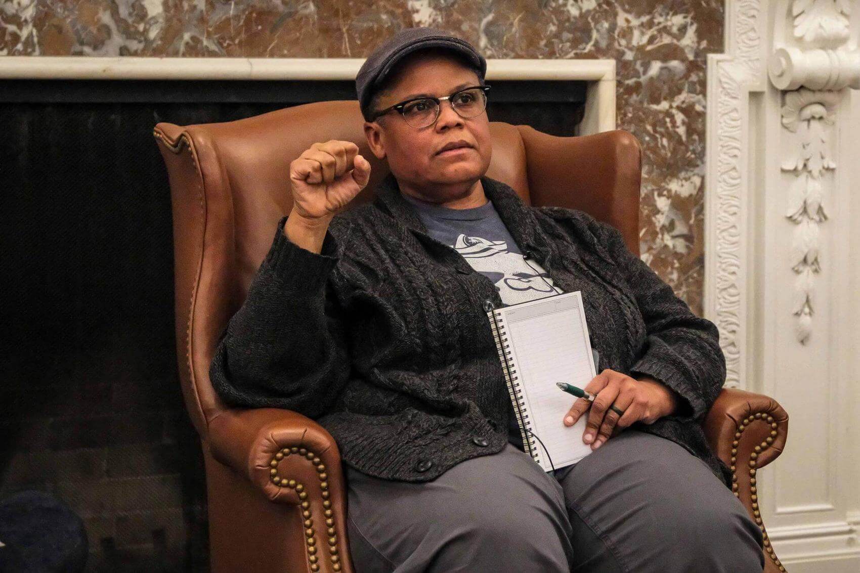 Audience seated in rows, some with notepads, in a conference or meeting setting.