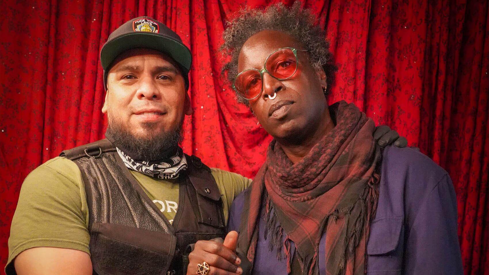 Person working on a colorful canvas against a brick wall with dim lighting.