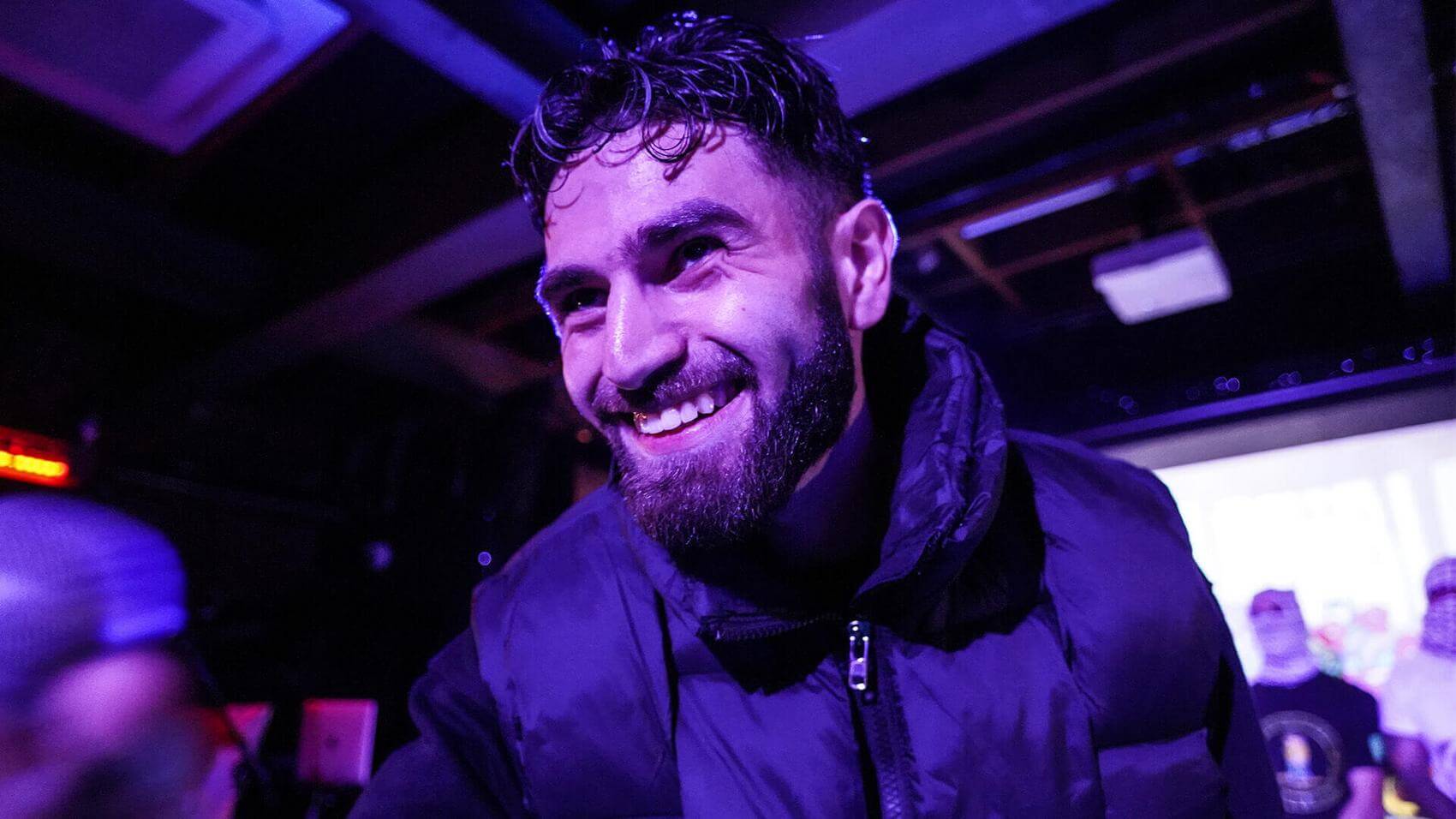 Two performers with microphones sing on stage; a DJ is visible in the background.