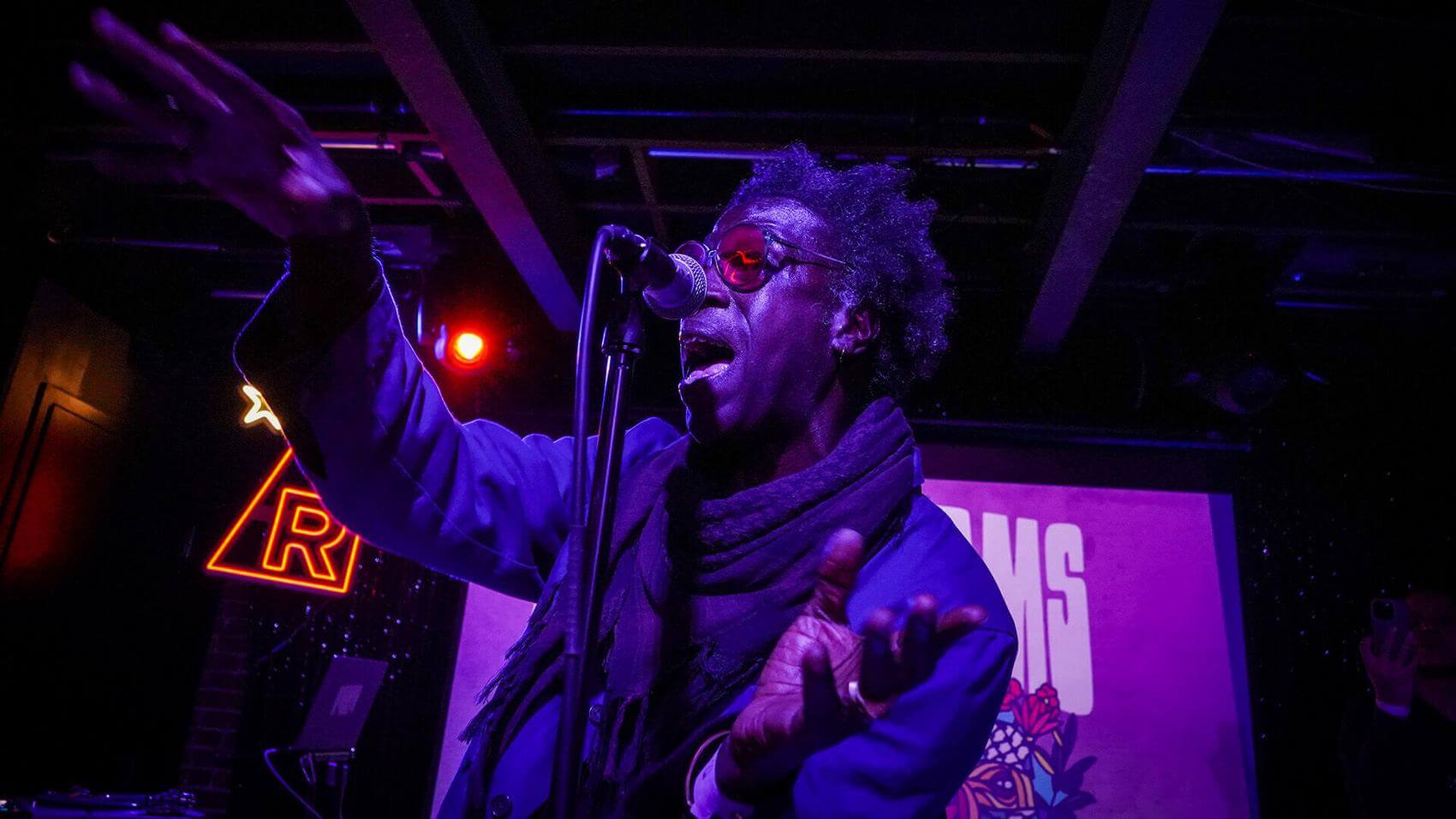 Two individuals pose together in front of a red fabric backdrop.