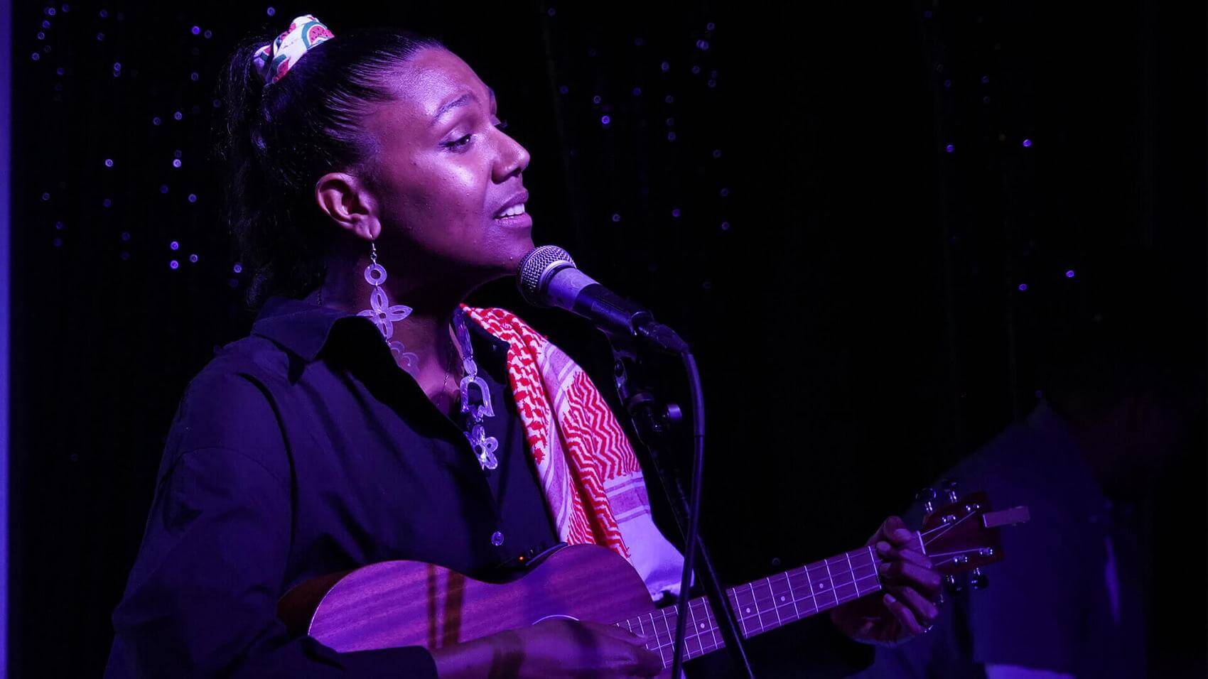 Person smiling and extending hand in a dimly lit venue with purple lighting.