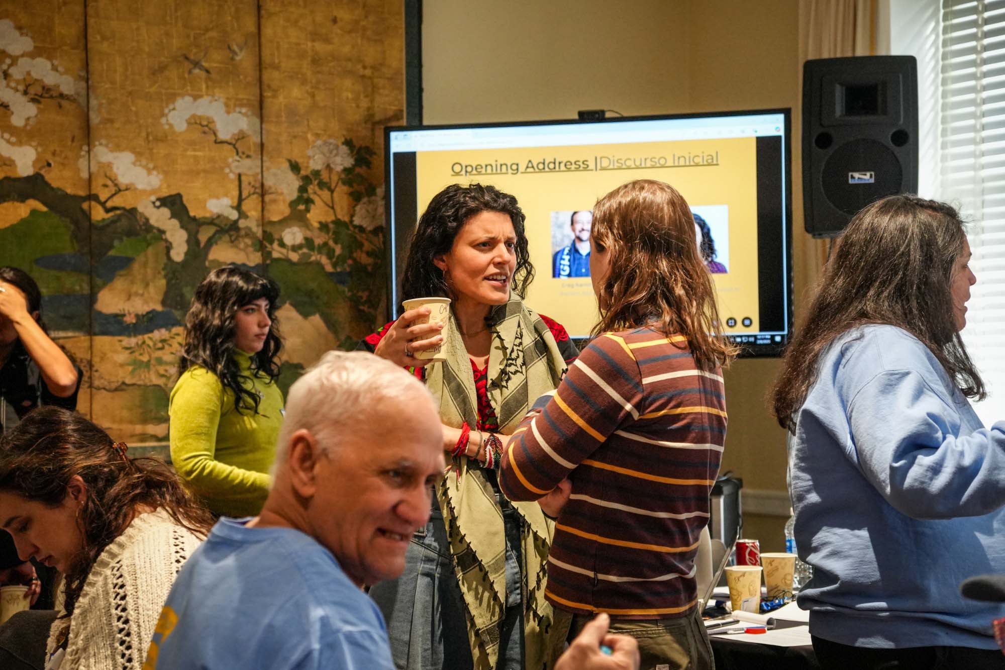 Group discussion in a room with a presentation screen, cups in hand.
