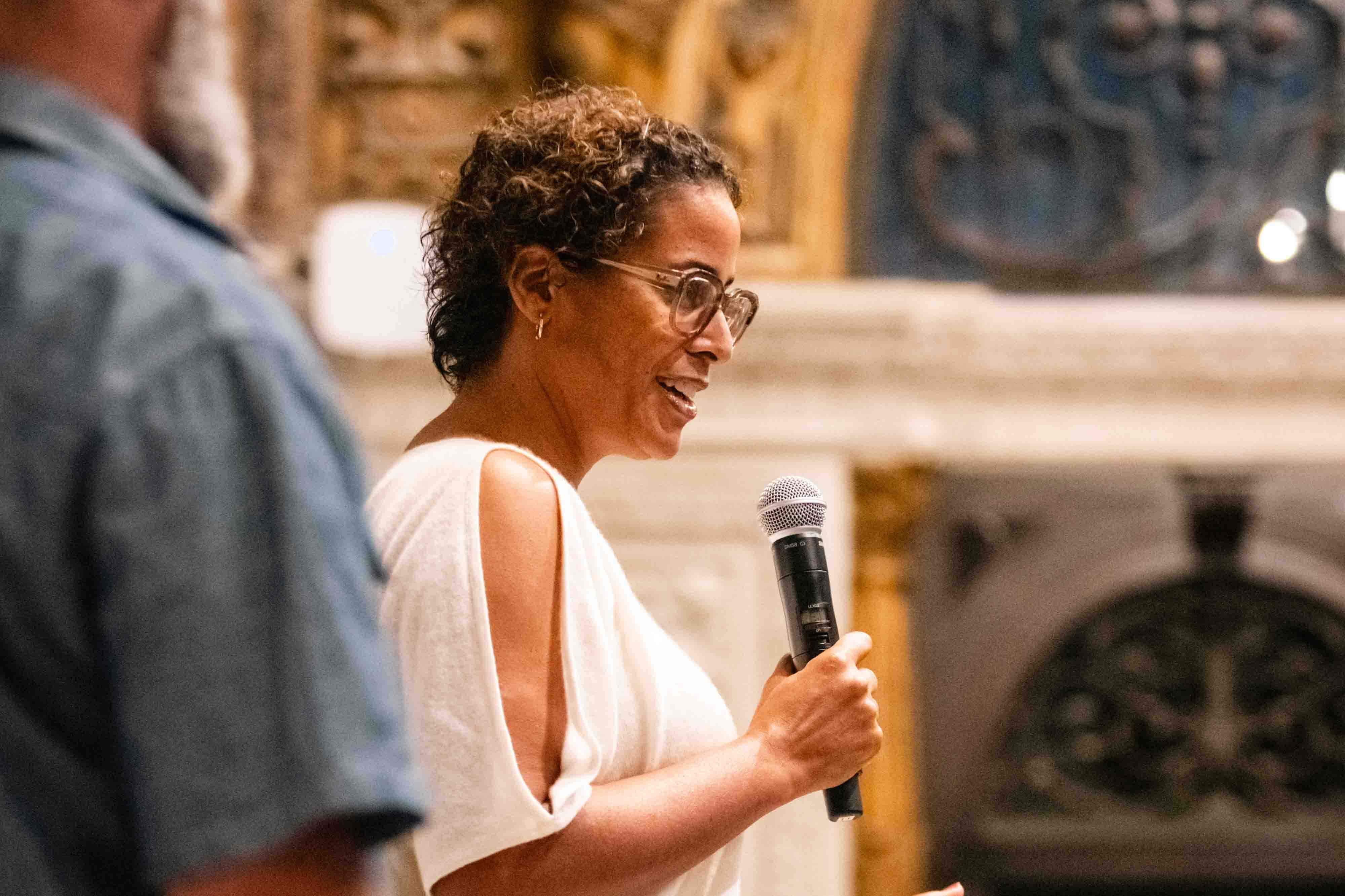 Man gesturing with hands while speaking on stage against a colorful background.