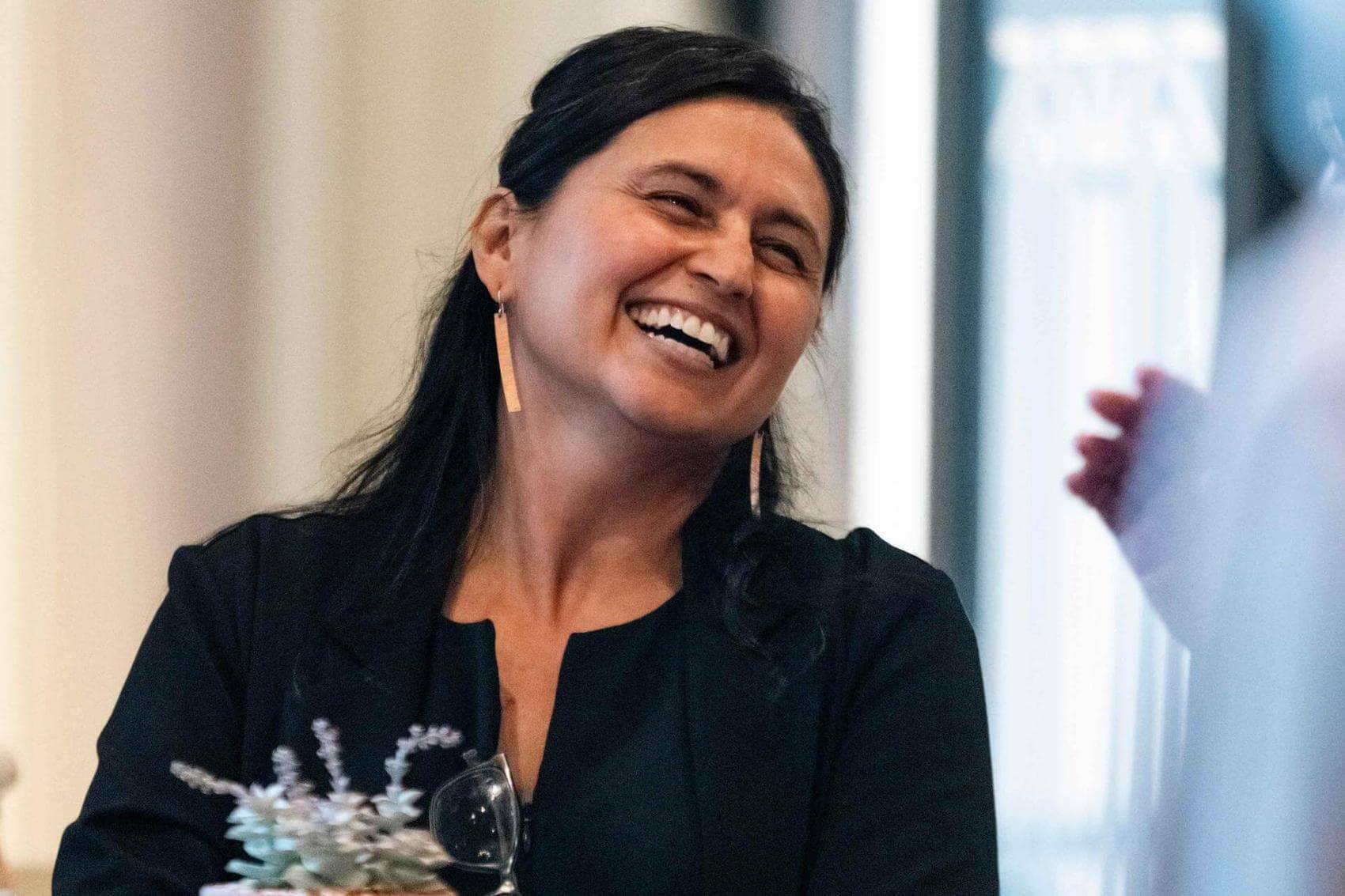 Person speaking into a microphone, with a blurred figure in the background.