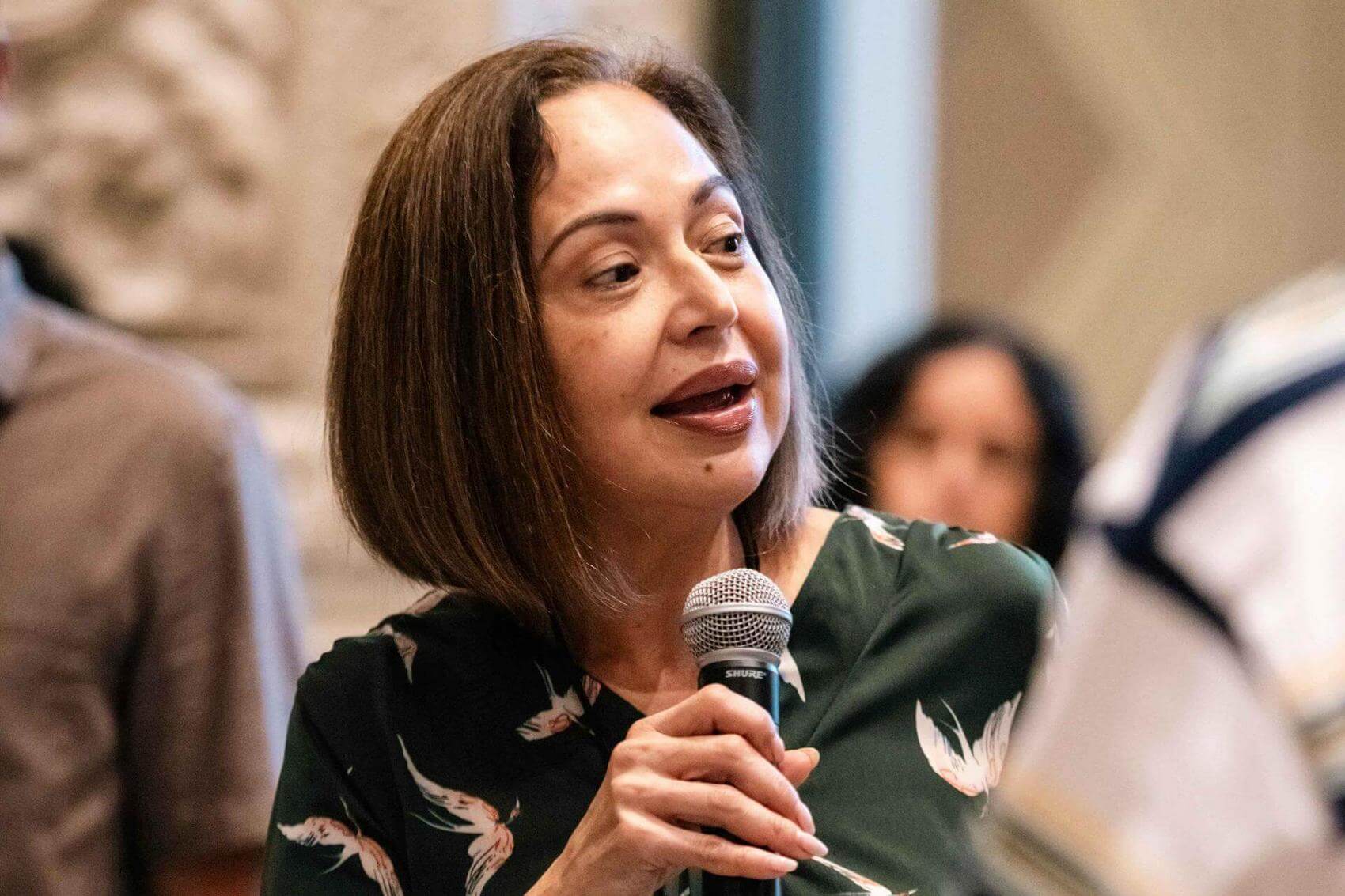 Smiling woman holds a small bouquet of flowers and interacts with another person.