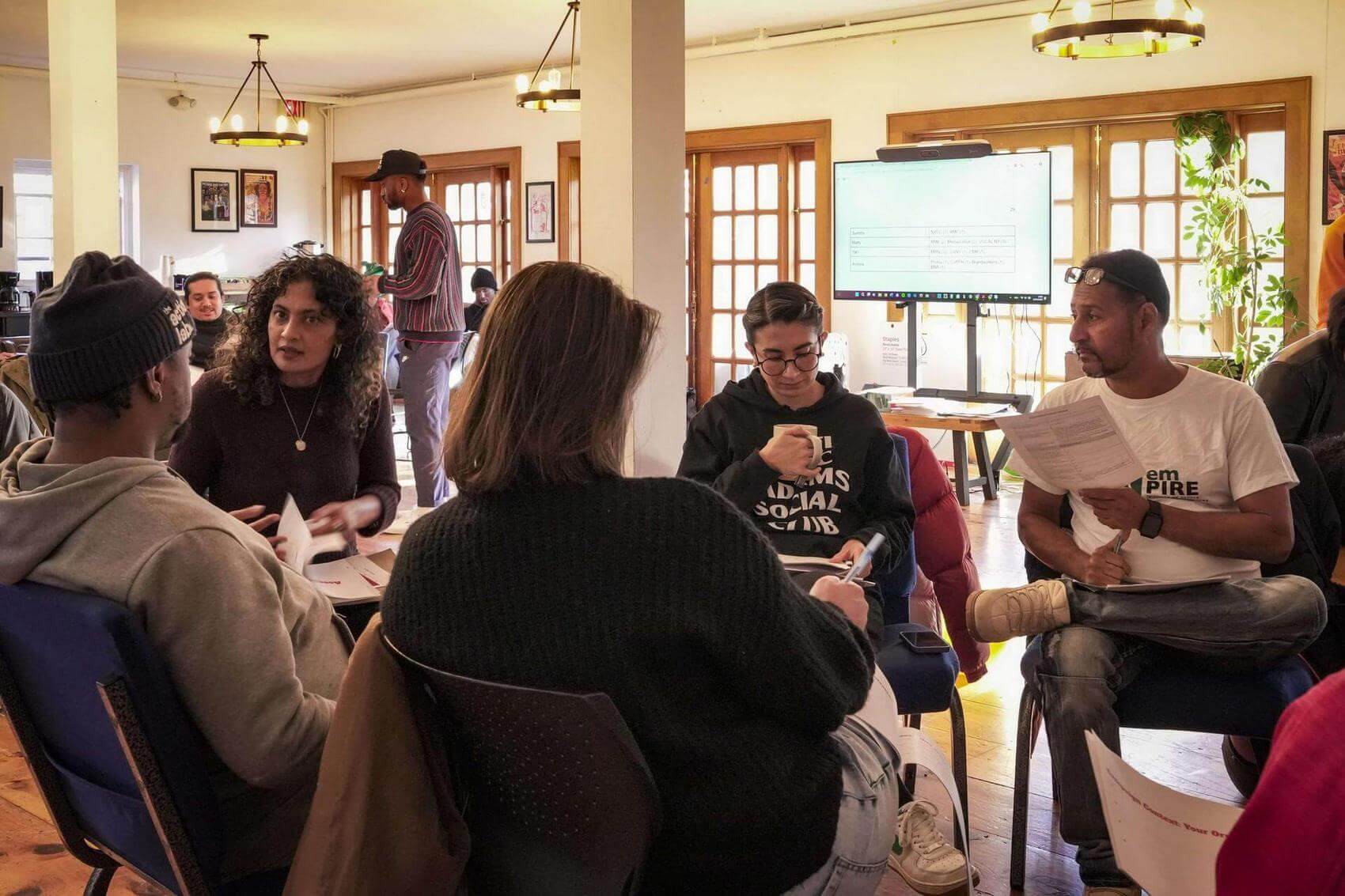 A group discussion in a room with people seated and engaged, some holding papers.