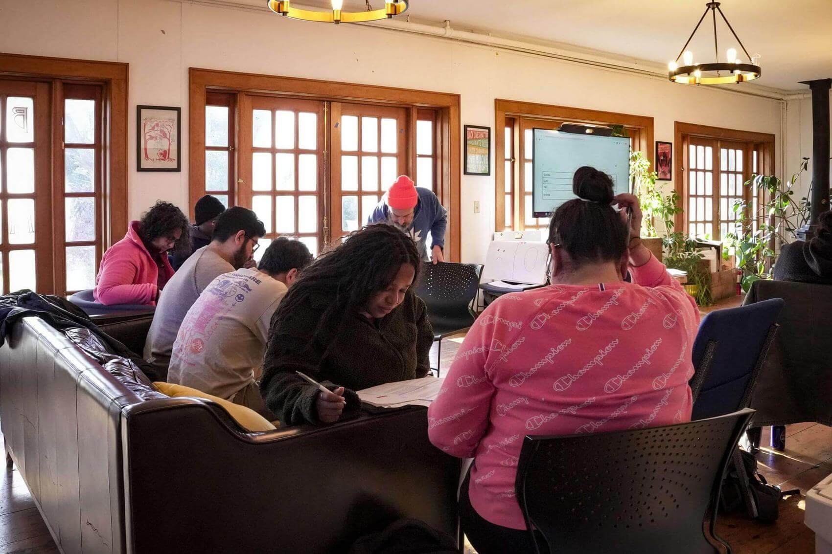 A group of people stands in a circle, listening to a speaker holding a clipboard.