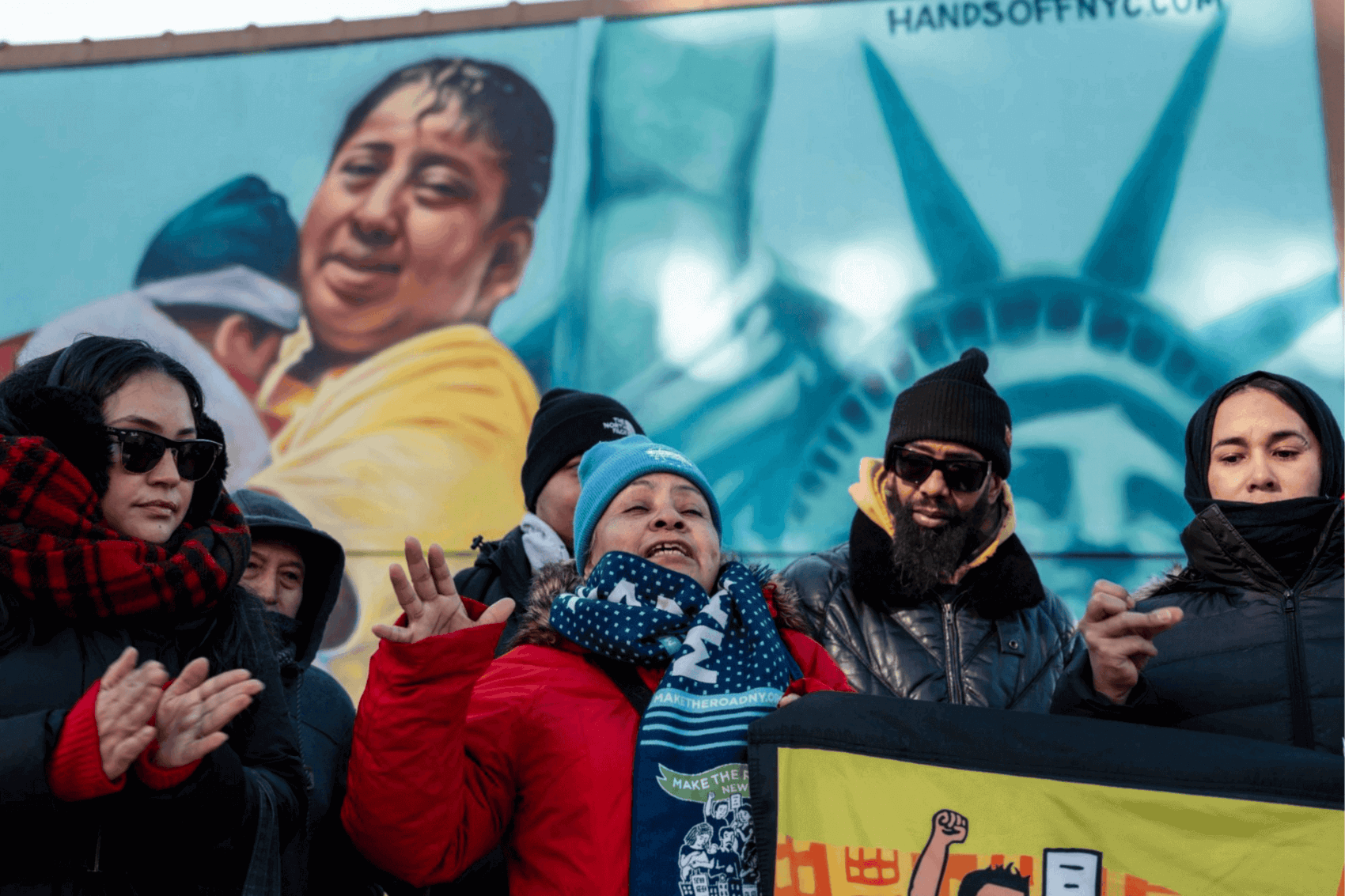 Mural of a person hugging a child with a city skyline and the Statue of Liberty in the background.