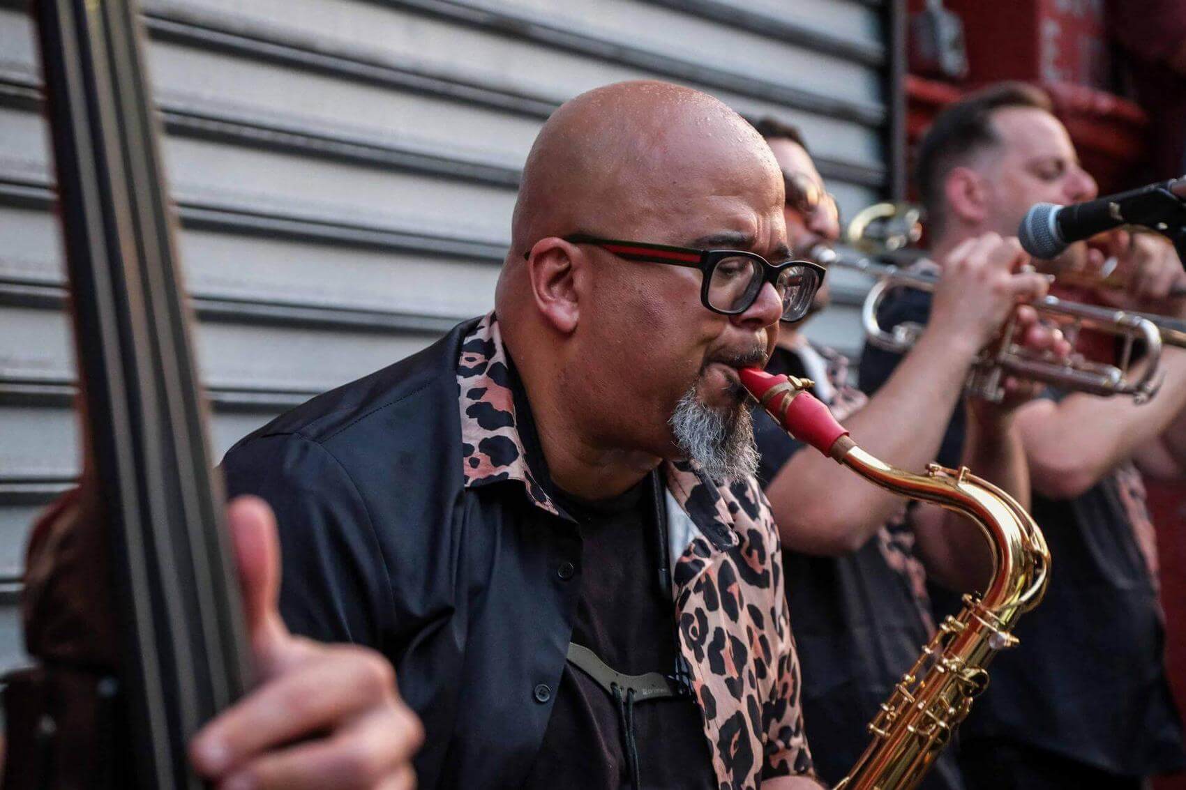 Musician playing a saxophone with a trumpet player in the background.
