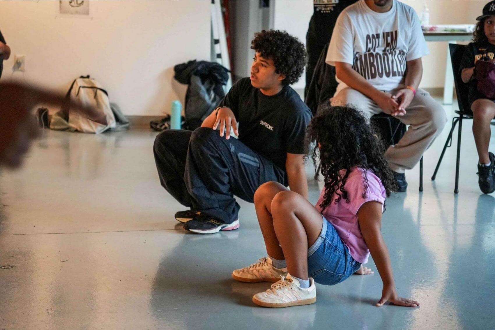 Three people gather around a DJ setup, examining turntables and equipment.