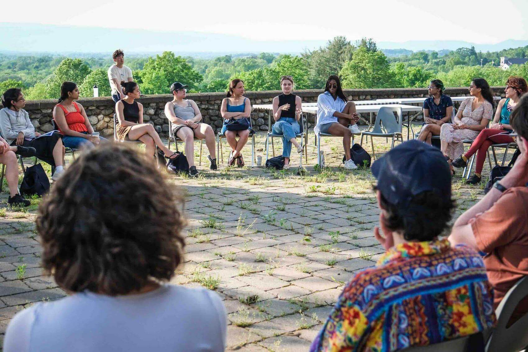 Group of people sitting at a long table outdoors overlooking a green landscape.