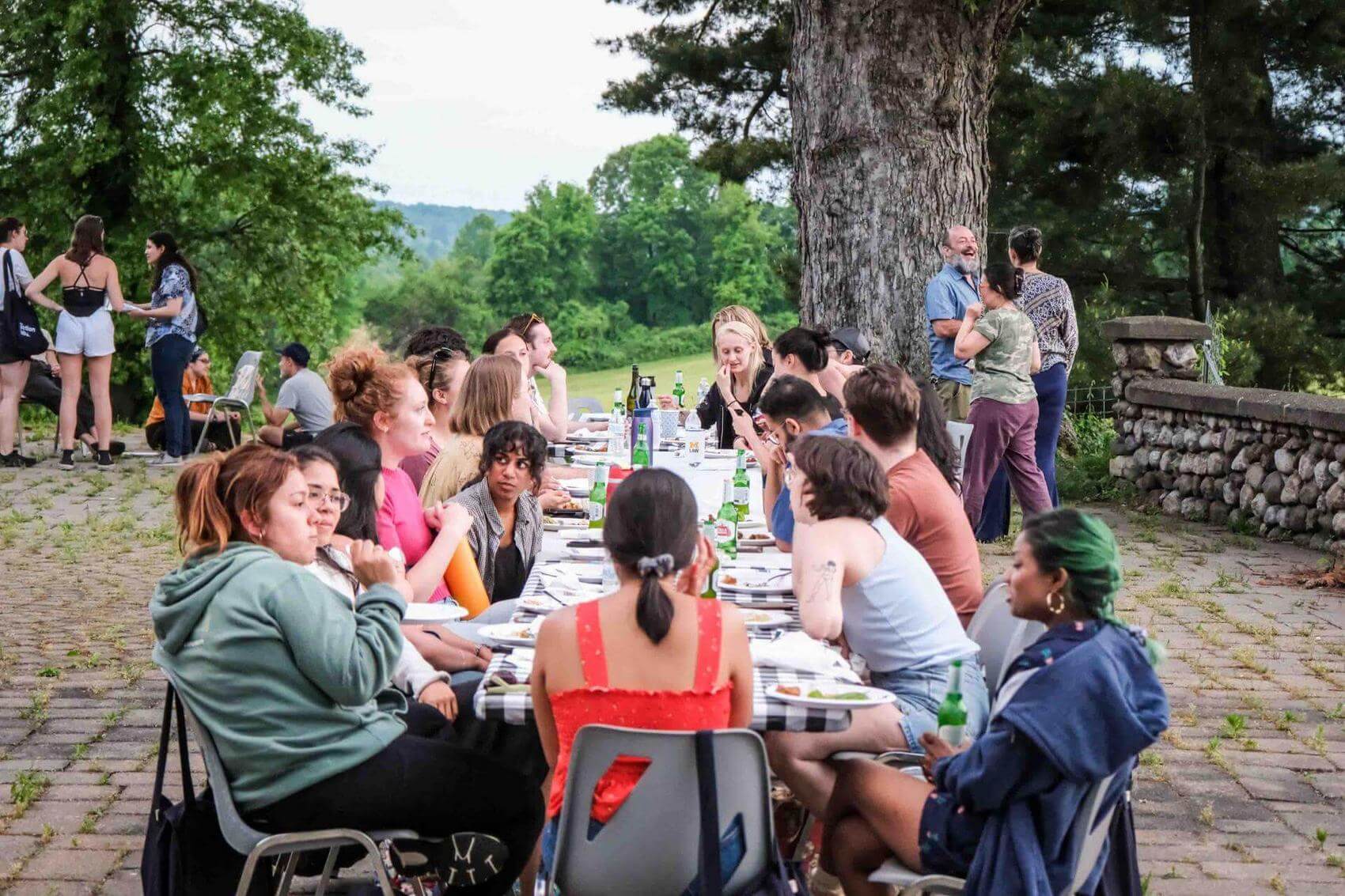 Eight individuals around a round table engaged in conversation, with notes and drinks present.
