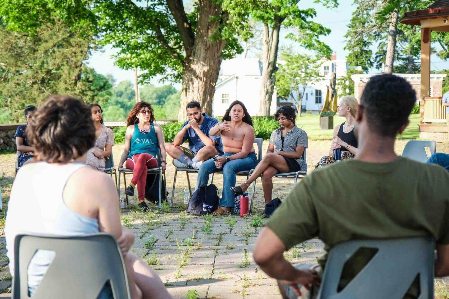 Group discussion in a spacious room with chairs arranged in a circle; two speakers at the front.