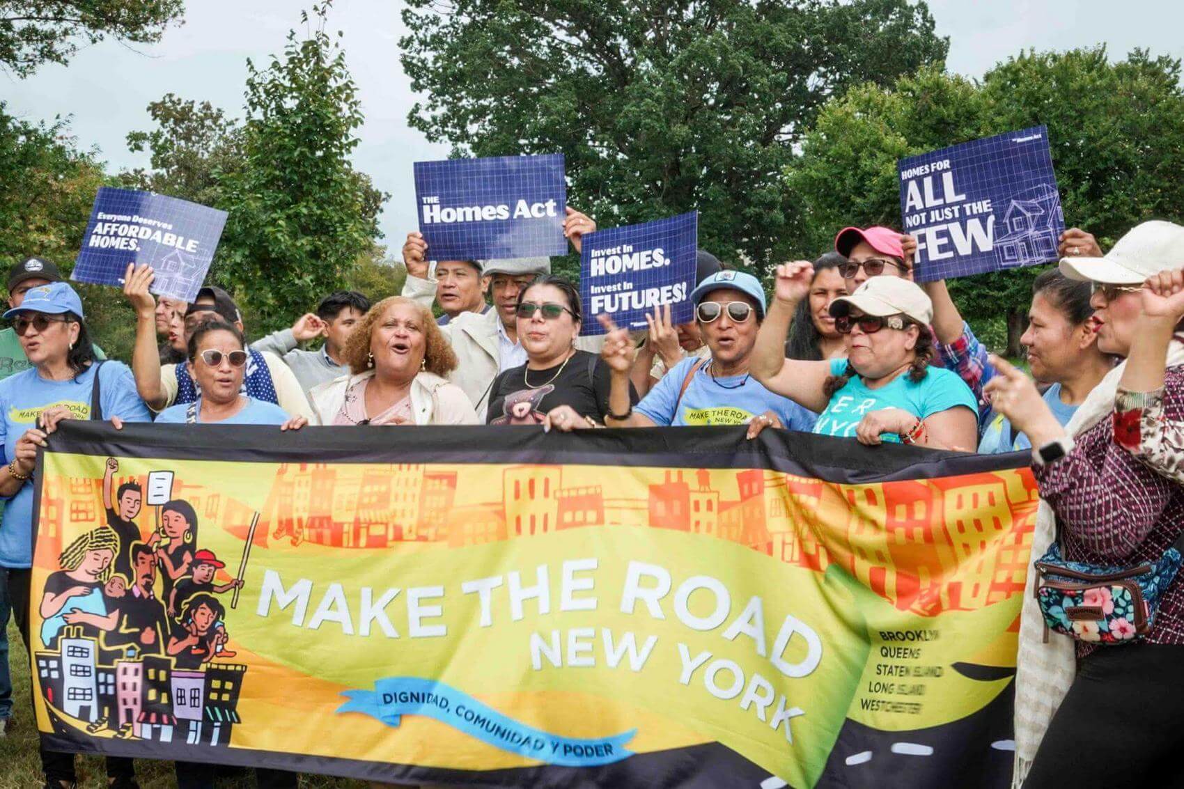 A speaker addresses an audience in a formal setting, with attendees sitting at round tables.
