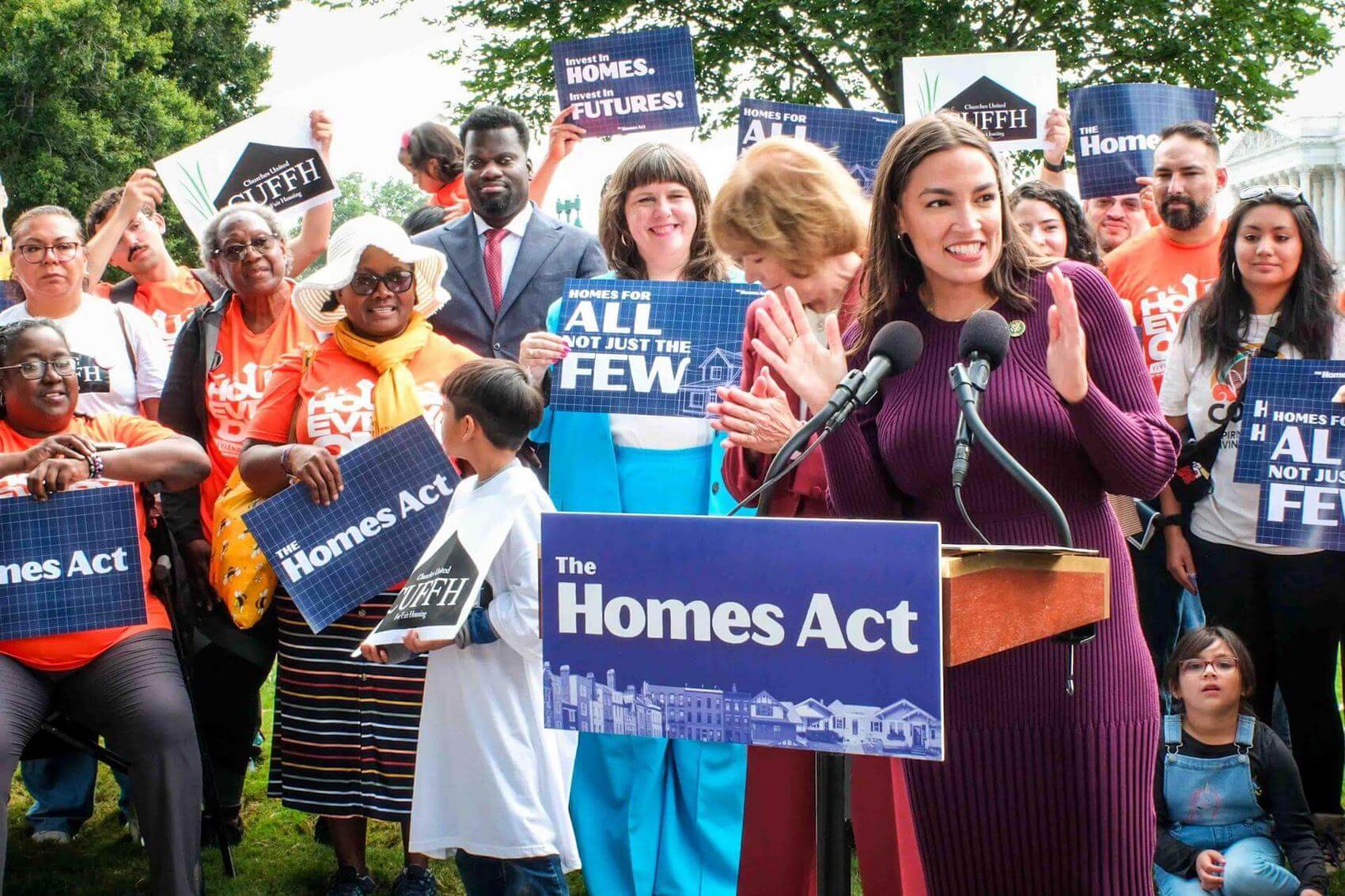 Three people in orange shirts pose together, smiling and raising arms in celebration.