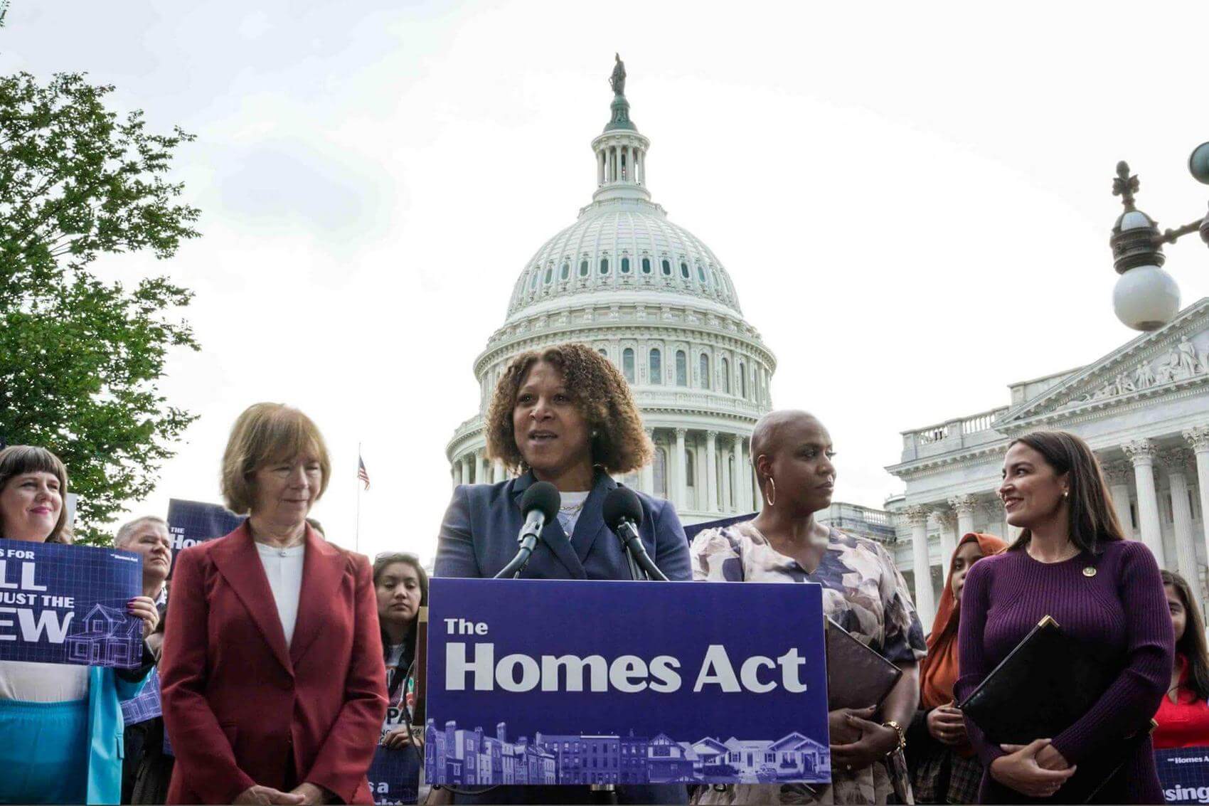Group of people in yellow shirts clapping at a meeting, with a screen displaying "Housing is a Human Right."