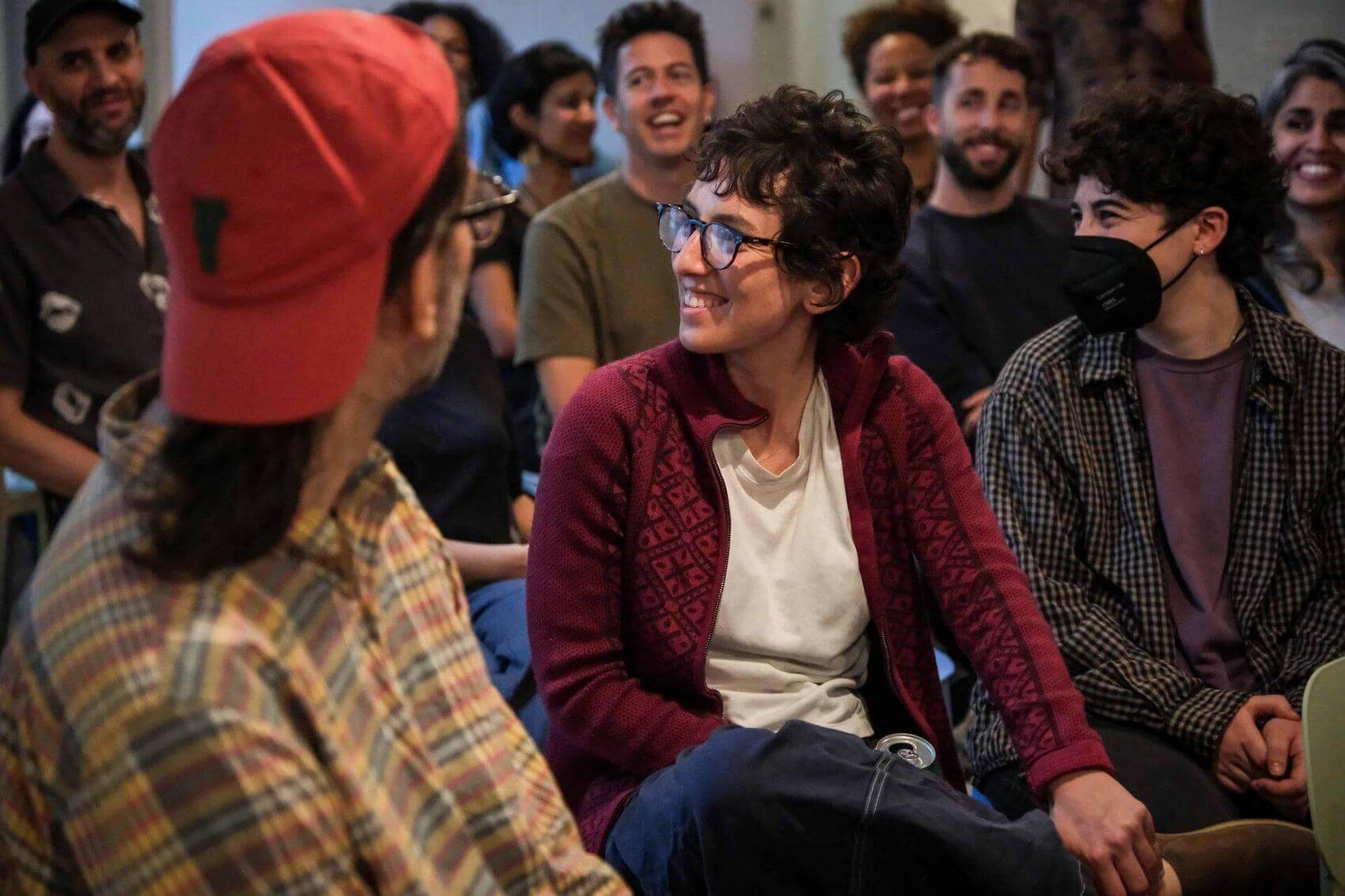 A group of people seated, some laughing and interacting, in a room with bookshelves.