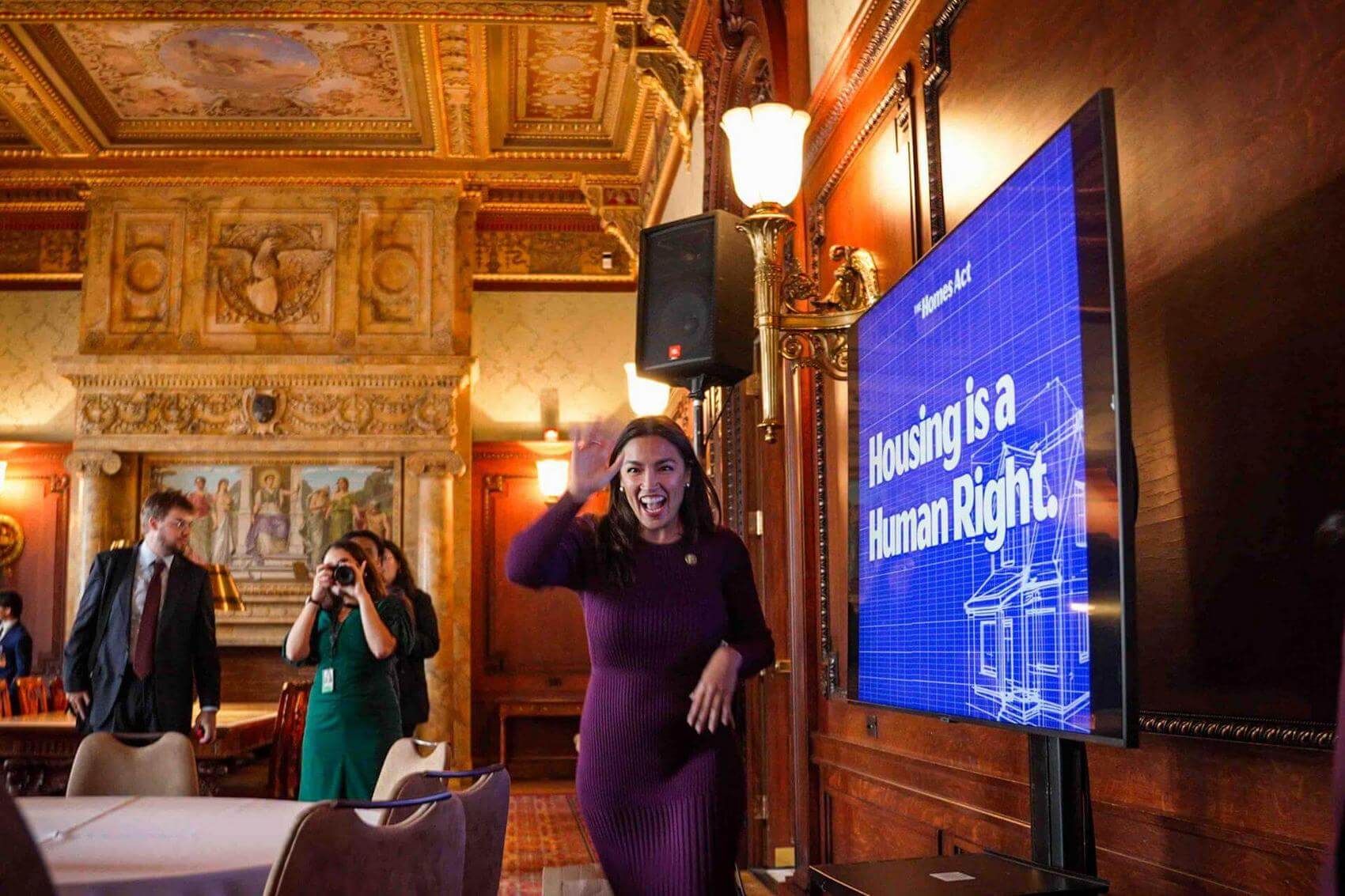 Group of people holding signs and banners, wearing orange shirts and hats at a rally.