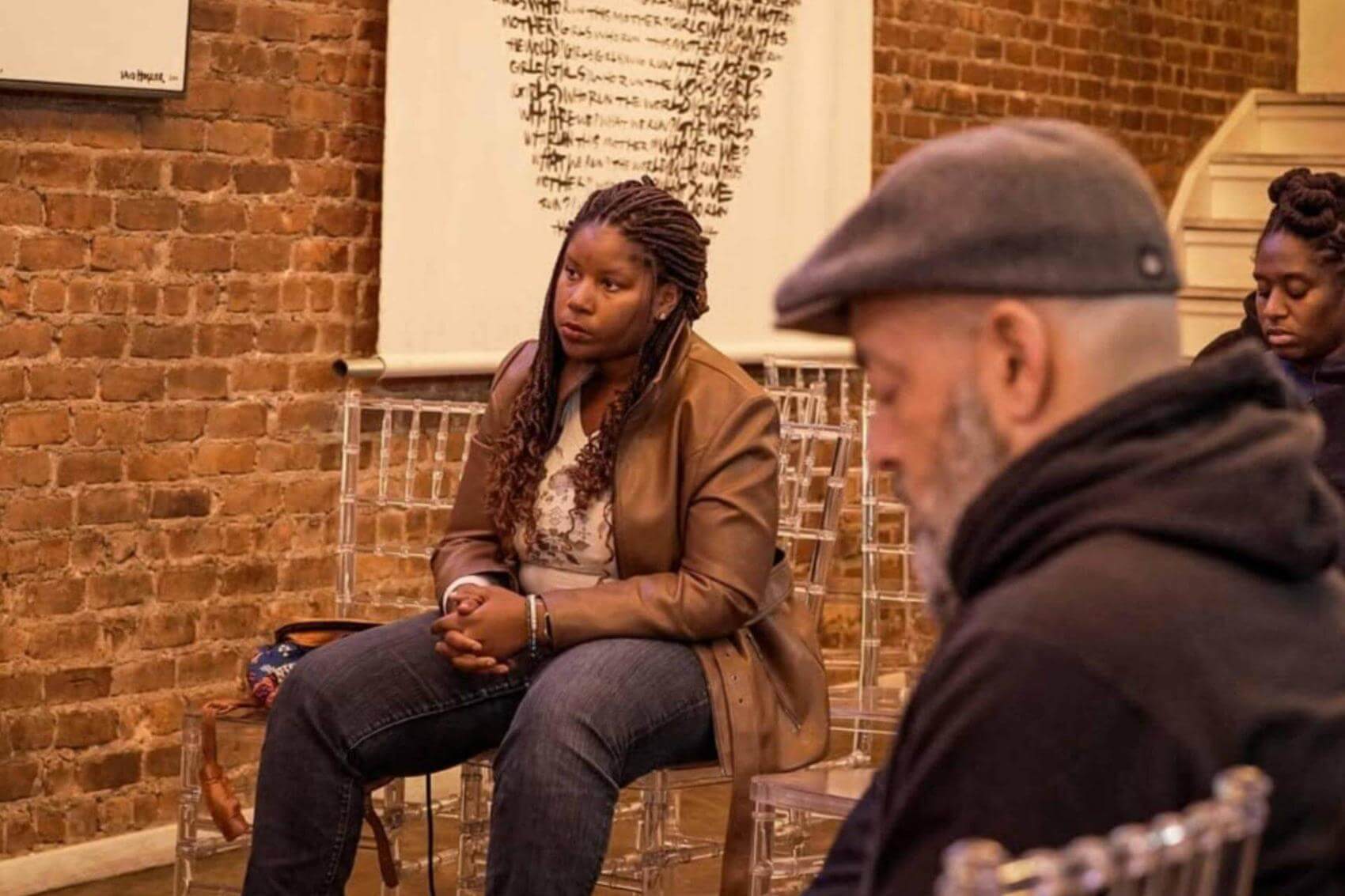 Person speaking into a microphone in front of a brick wall.