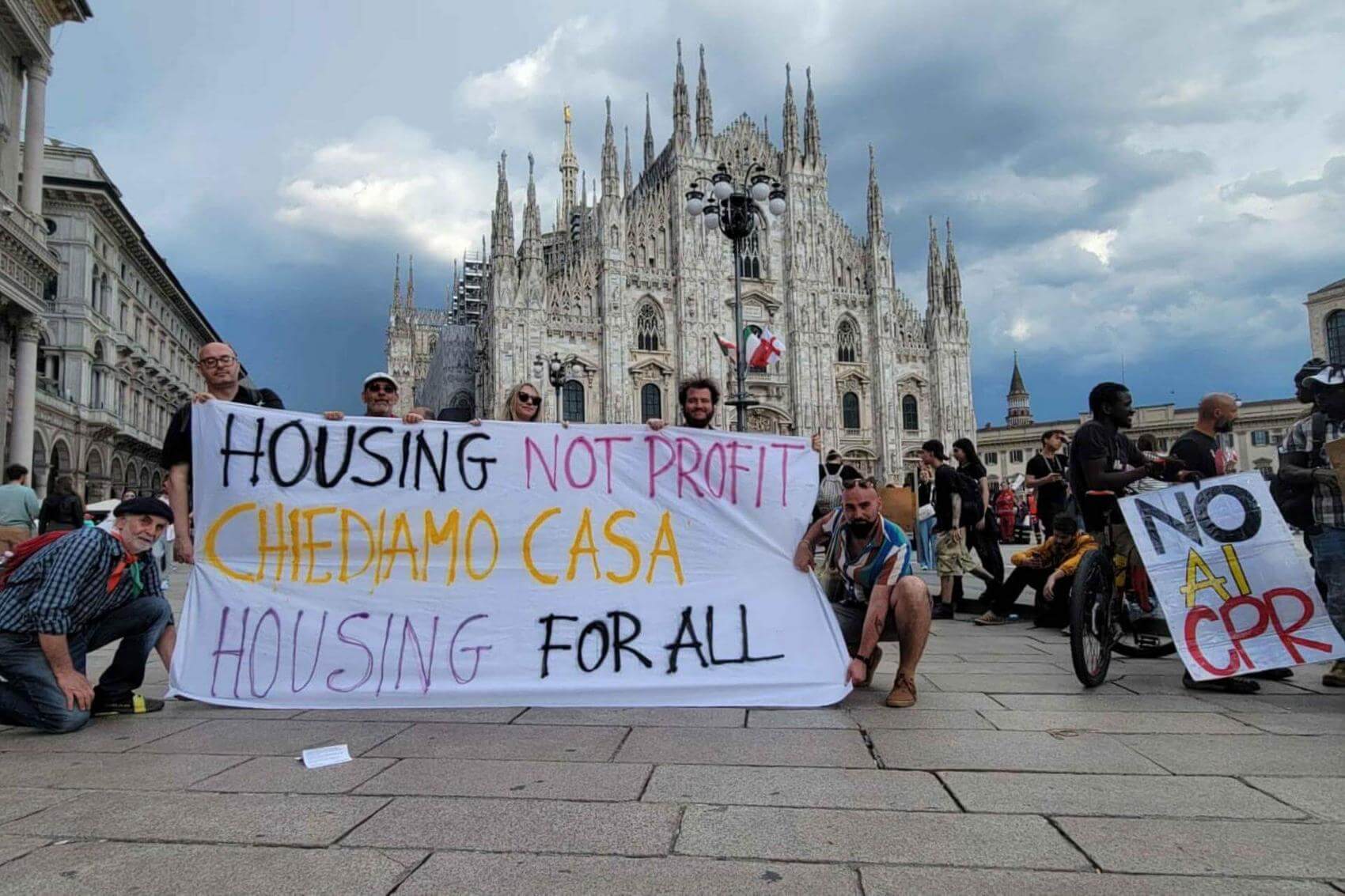 Four individuals hold signs with messages about housing rights, outdoors against a blue sky.