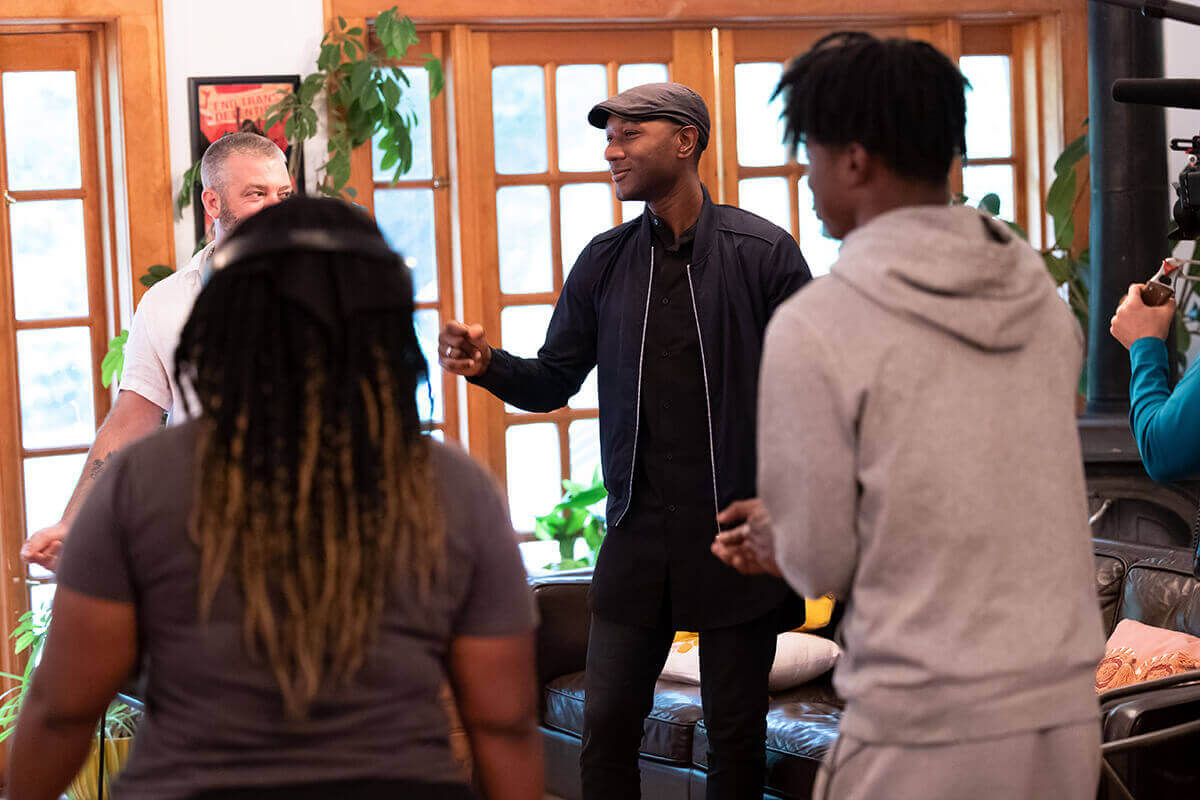 Four people standing indoors, two women facing two men, engaging in conversation or group activity.