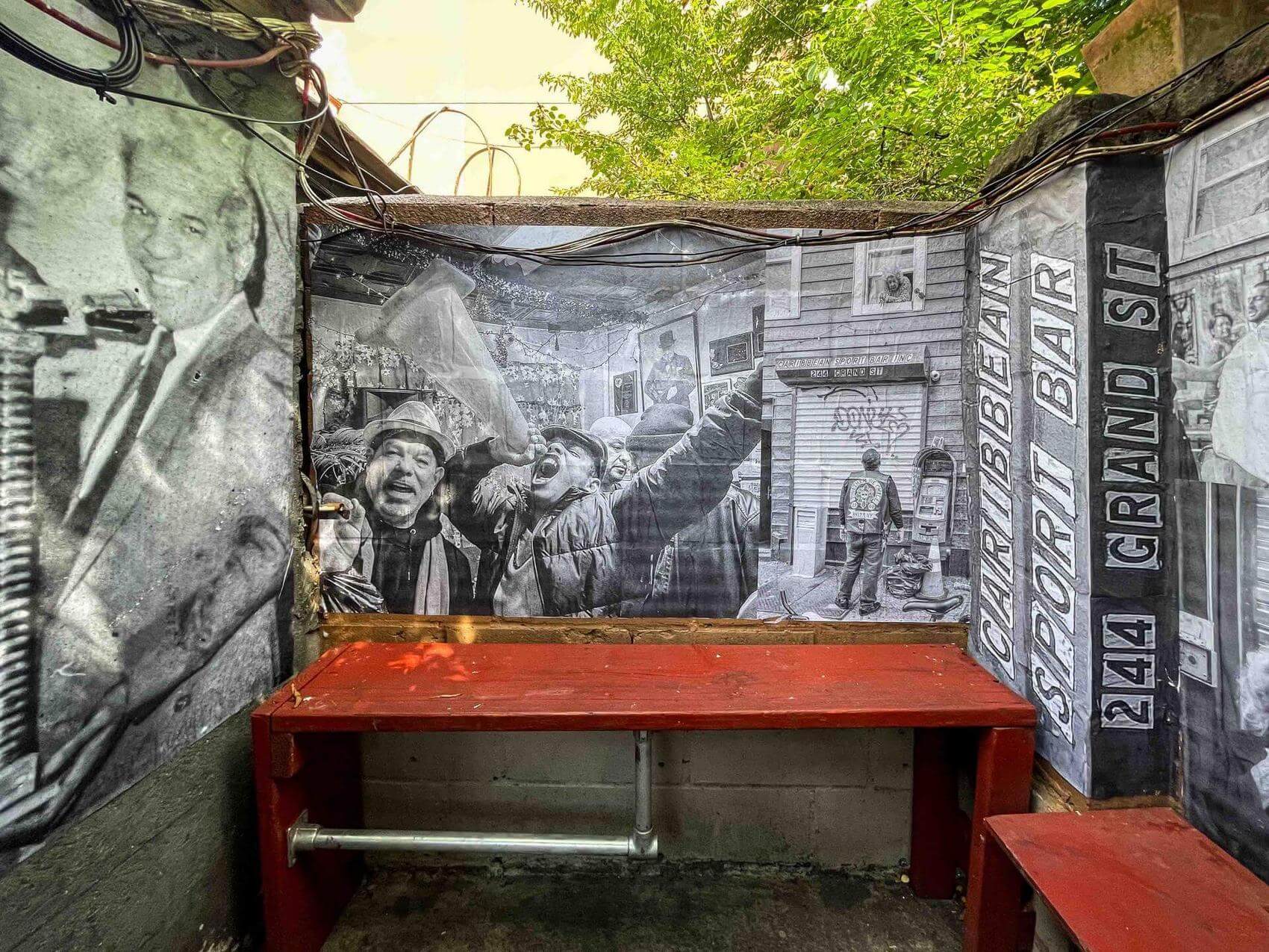 Mural-covered wall in an outdoor seating area featuring black-and-white photos and text.
