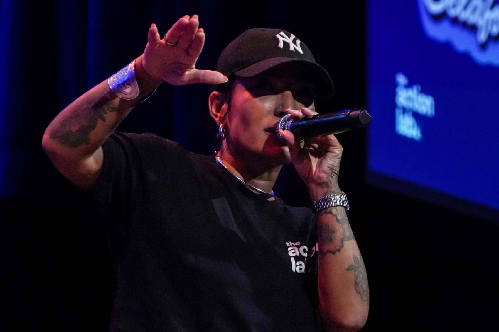 A performer speaks on stage in front of an audience, with a large screen displaying "COMMON 2025 Belong Fellow."